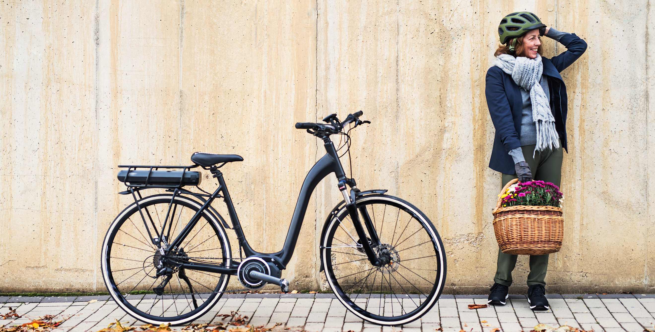 An older woman stands on the sidewalk with her e-bike.
