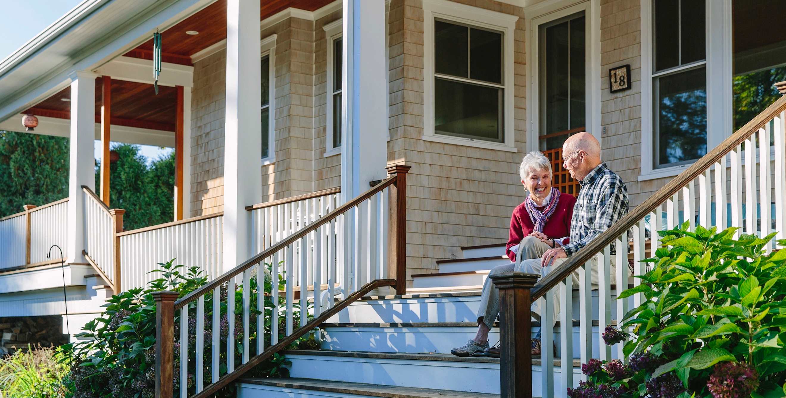 elderly couple sits smiling and laughing on the front steps leading to their home