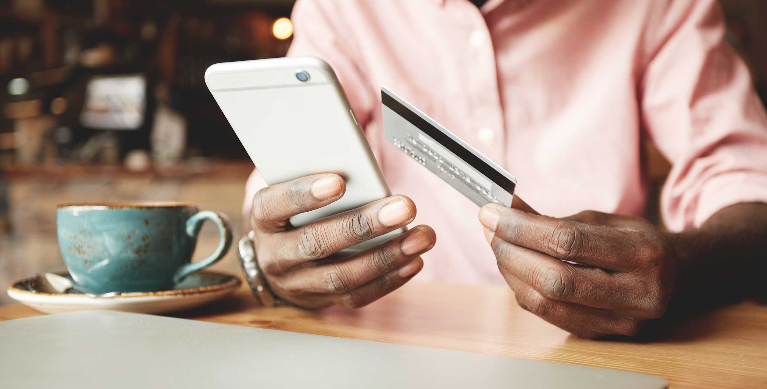 a black man uses a credit card to purchase something on his phone with coffee cup in foreground