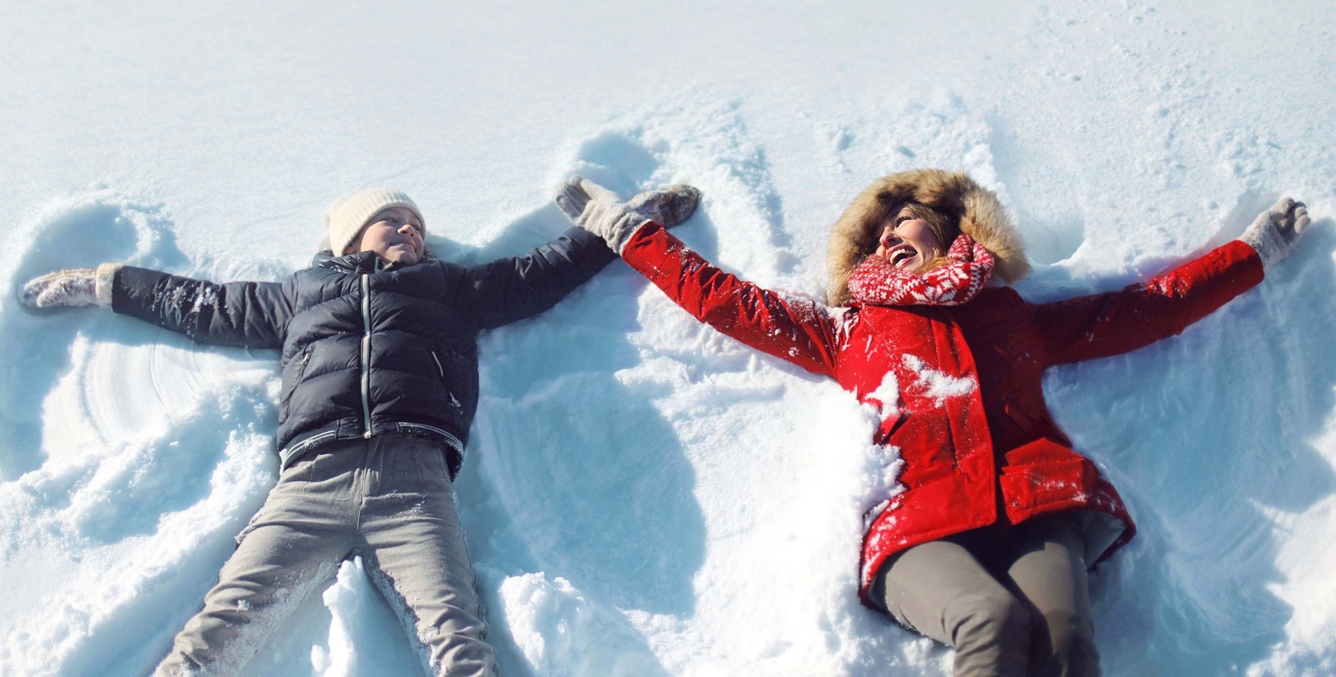 A mother and son make snow angles in winter coats.