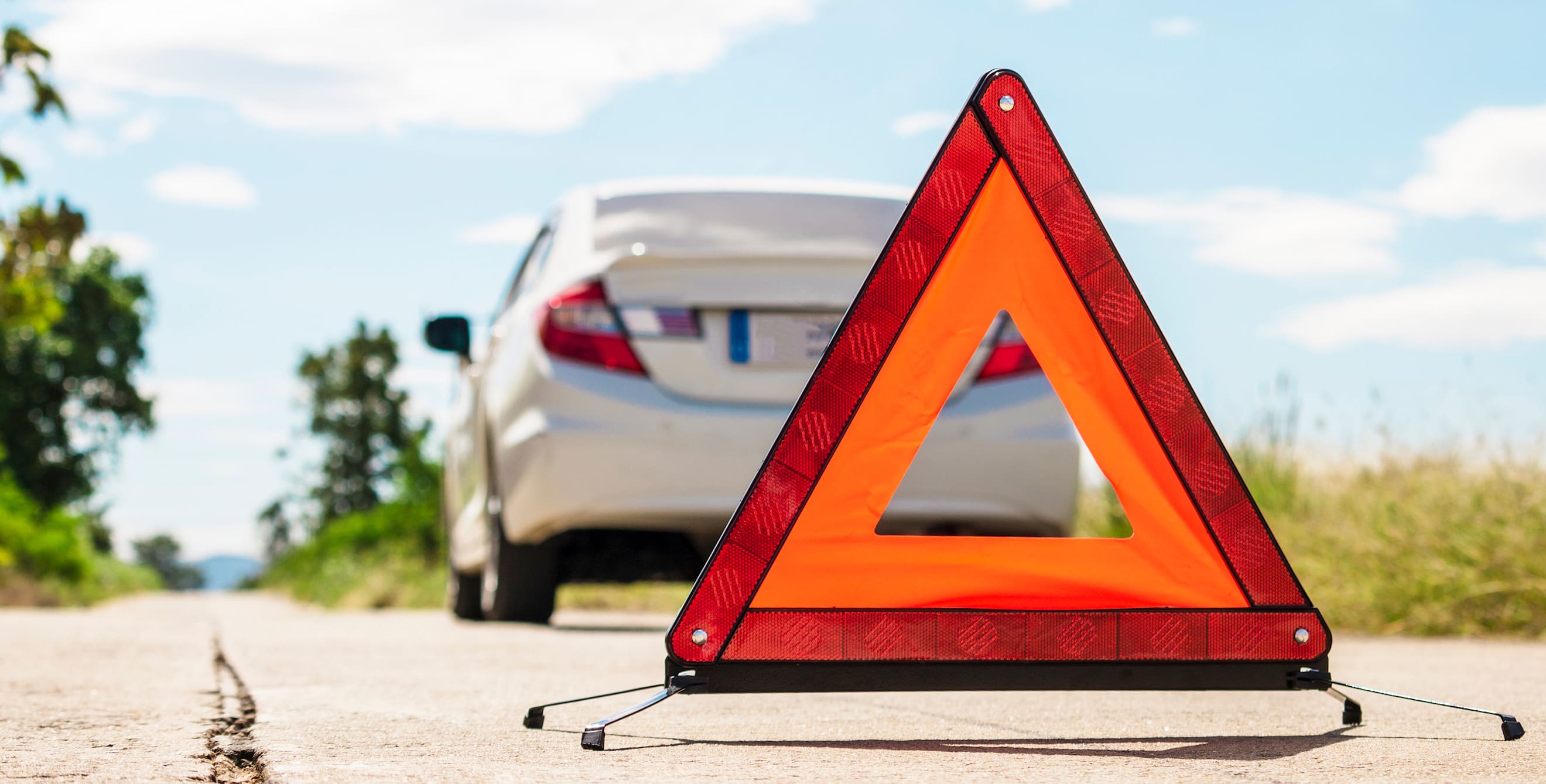 Emergency warning triangle in the road behind a broken down car.