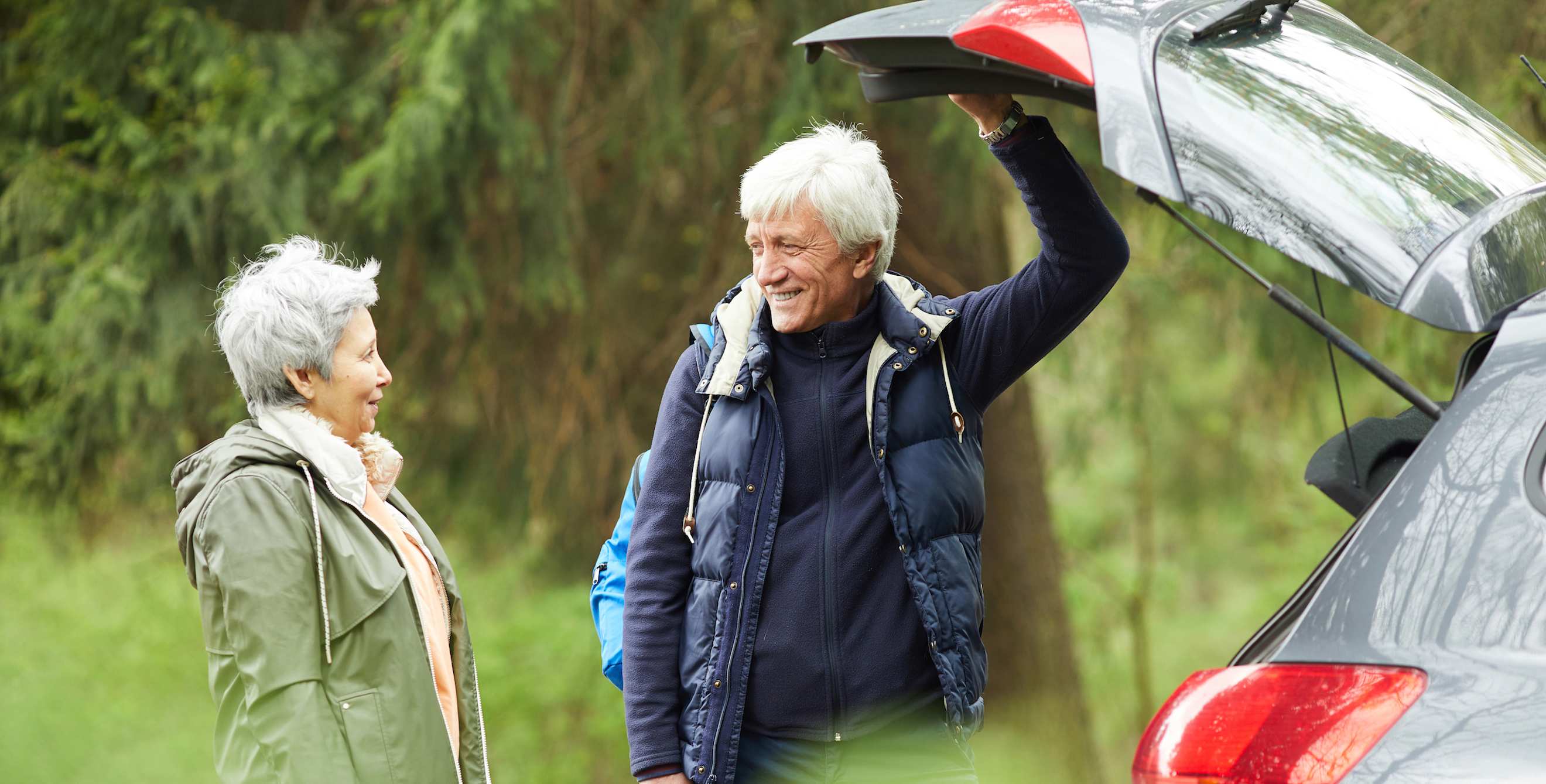 Happy senior couple opens the trunk of their car