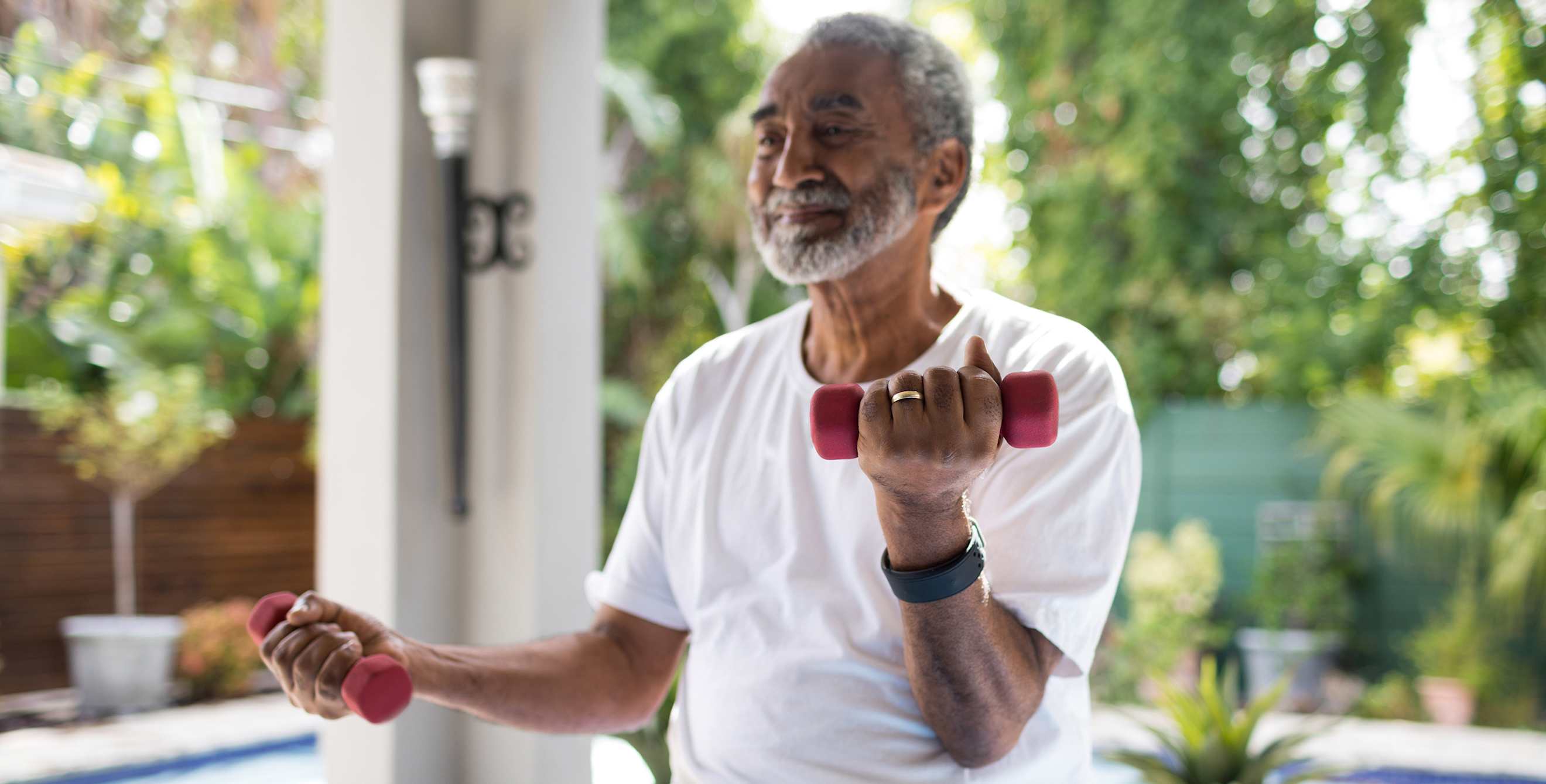 A senior man lifts weights in the backyard.