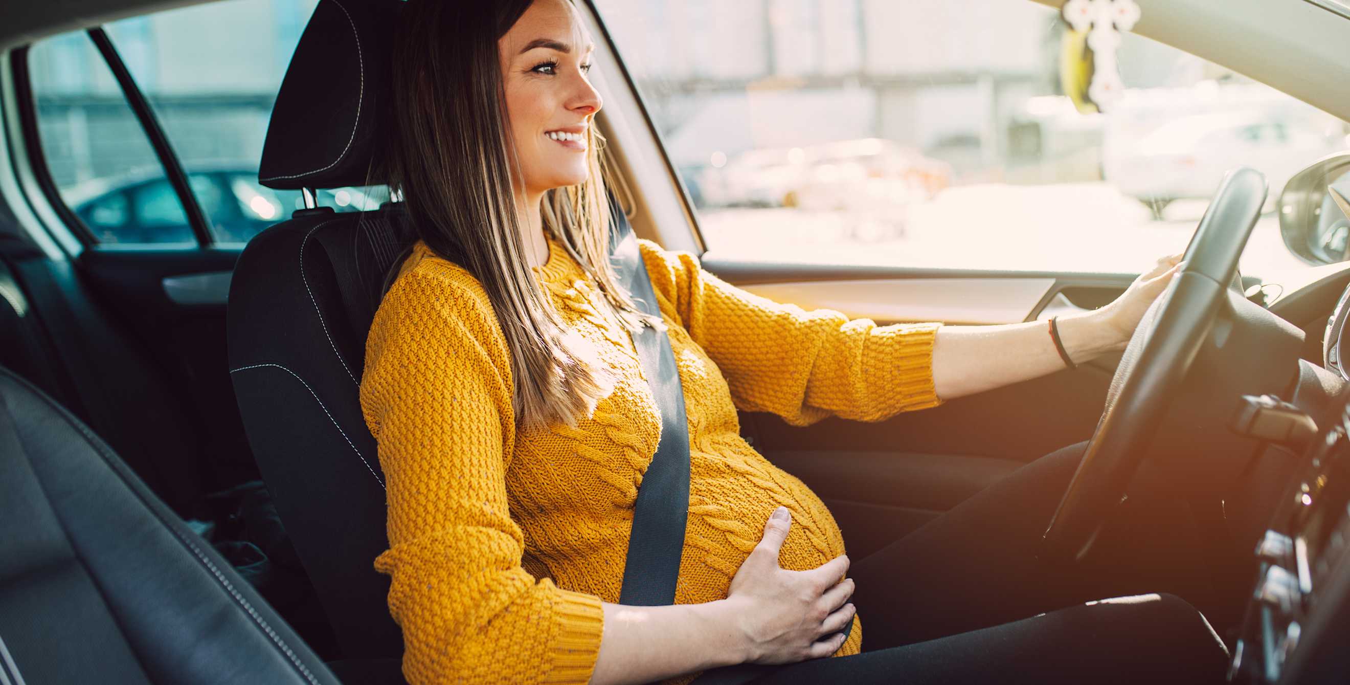 A pregnant woman drives her car.