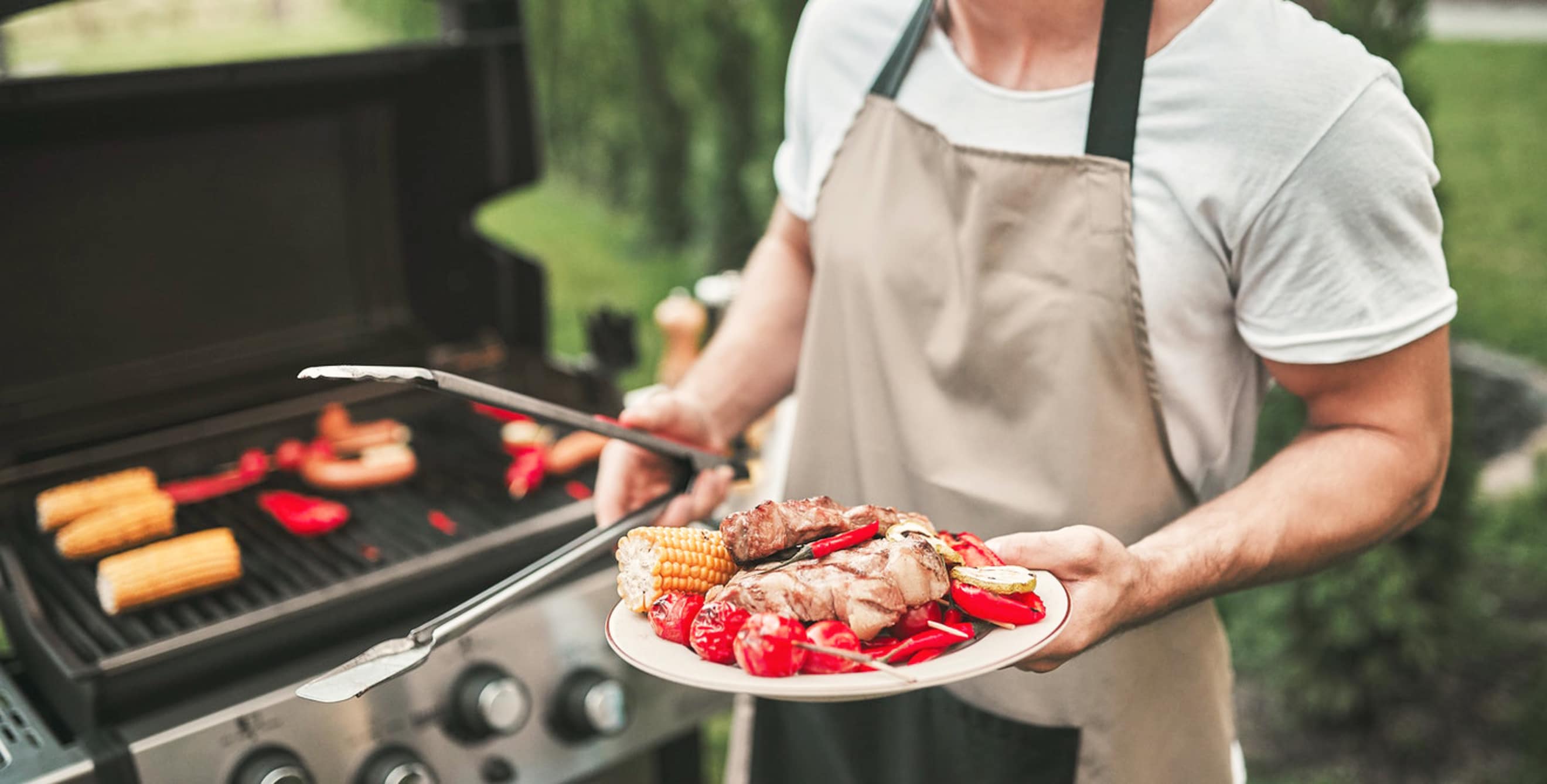A home chef holds a plate of freshly grilled meat and vegetables.