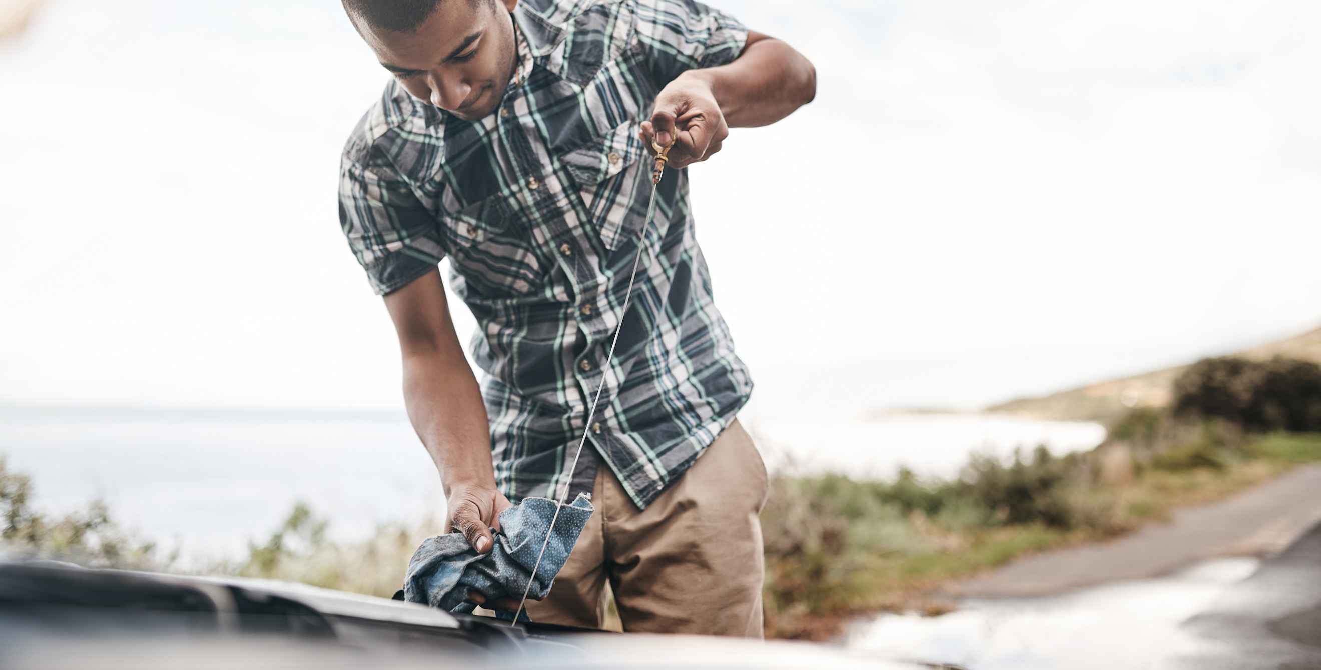 A man checks his oil on the side of the road.