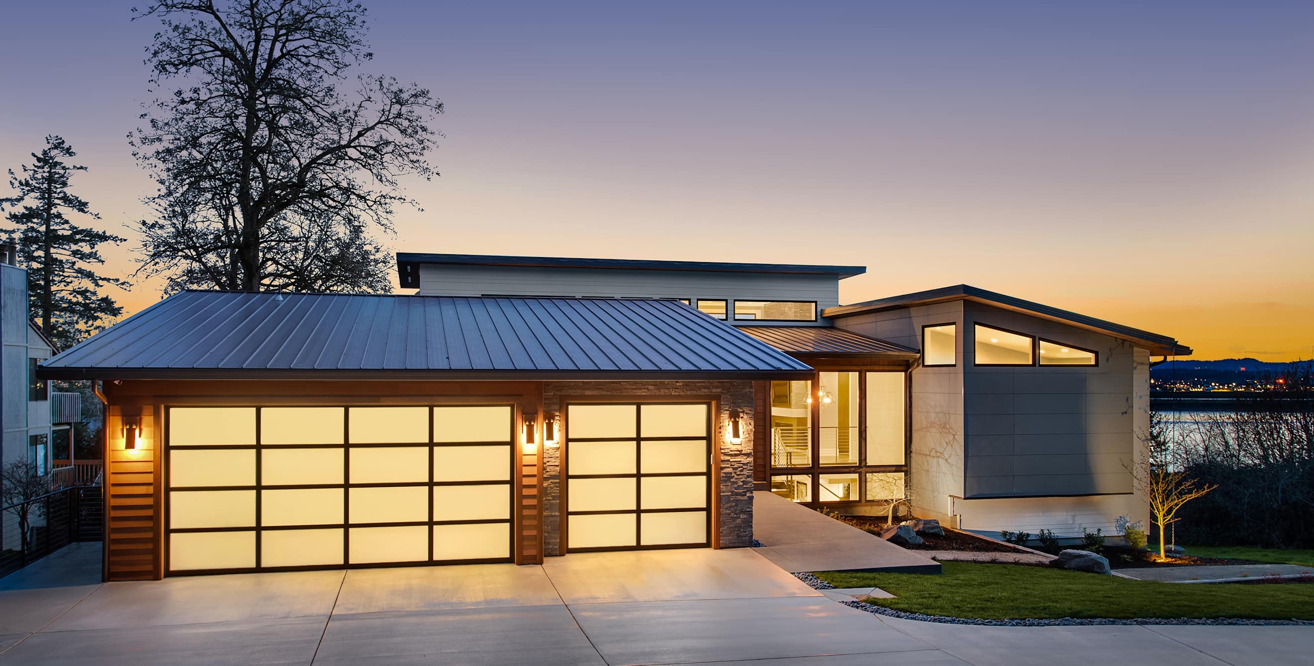 A modern lakeside home lit up at sunset.