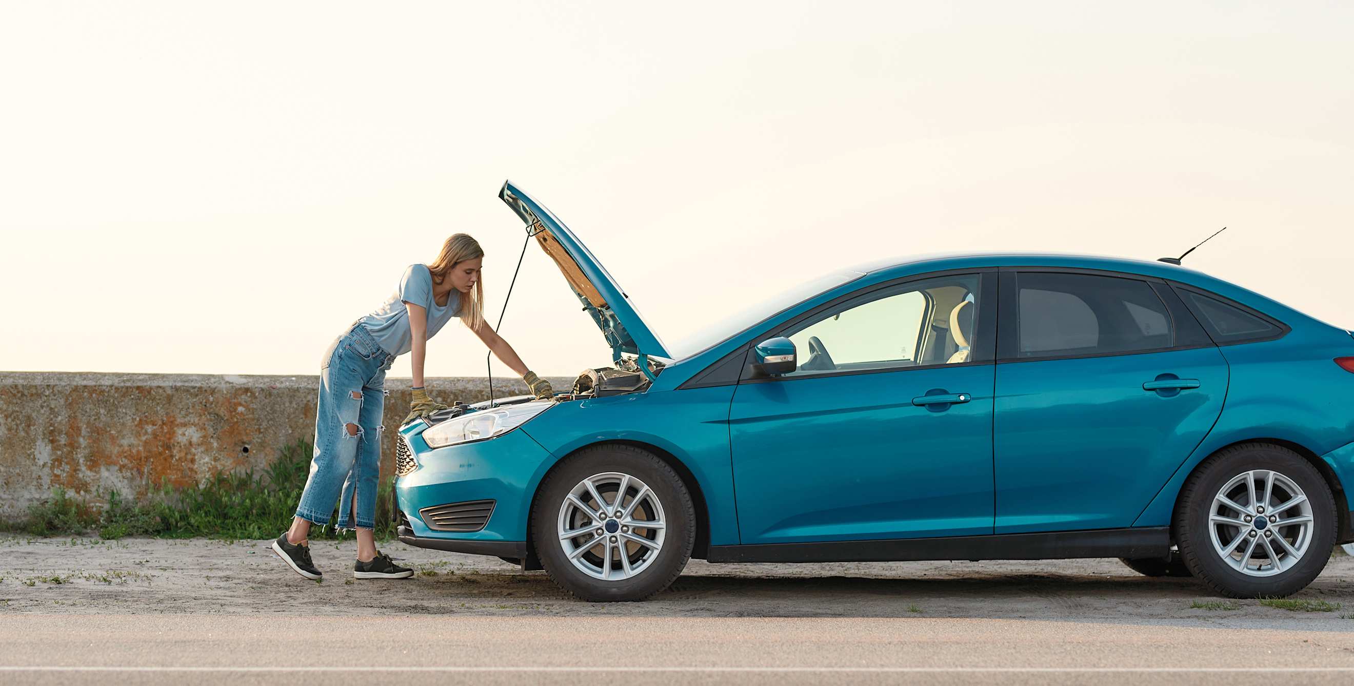 A woman looks under the hood of her overheated car.