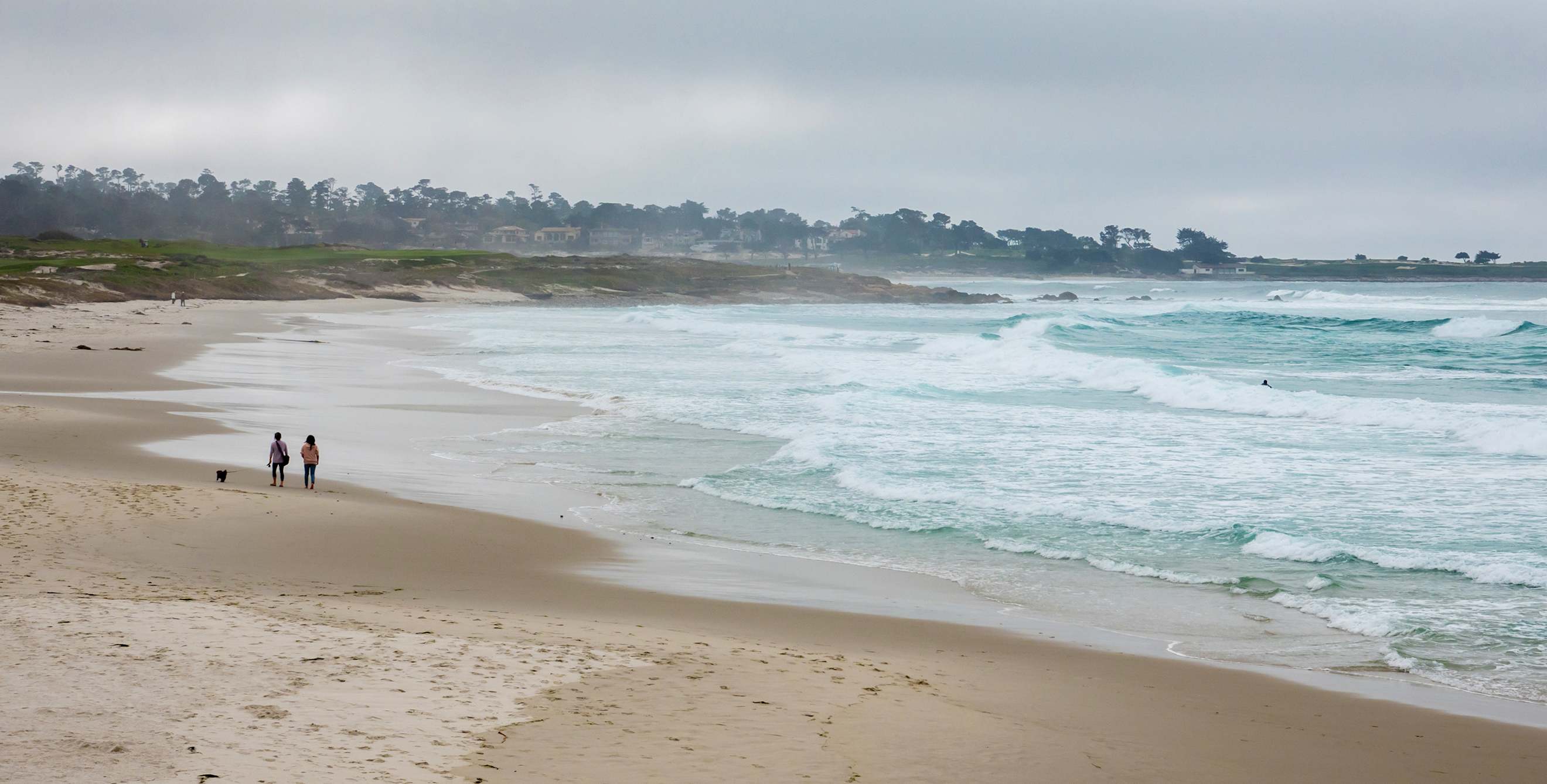 A couple walk on Asilomar Beach in Pacific Grove, California on a gray day.