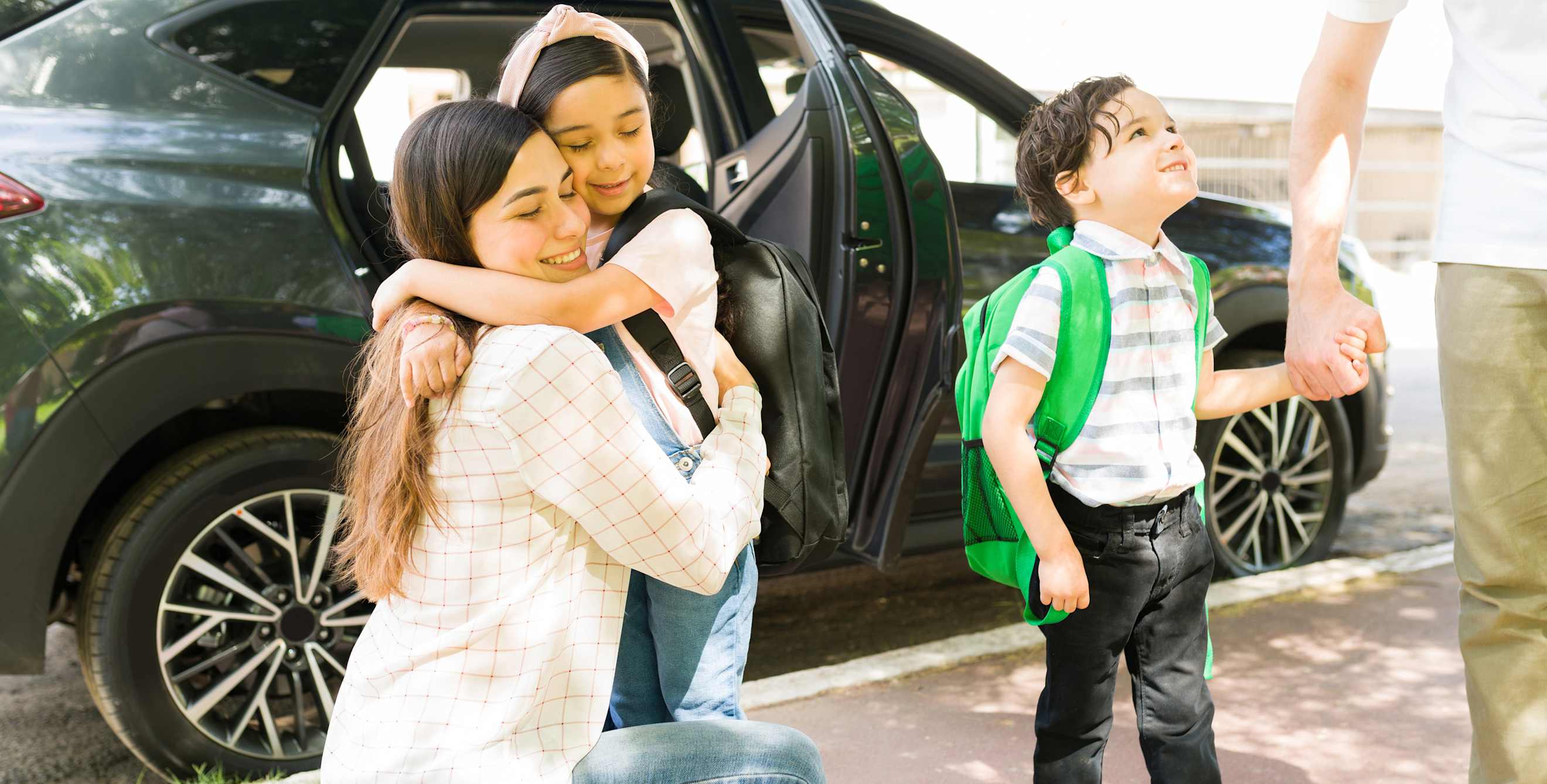 A mom hugs her daughter at school drop-off.