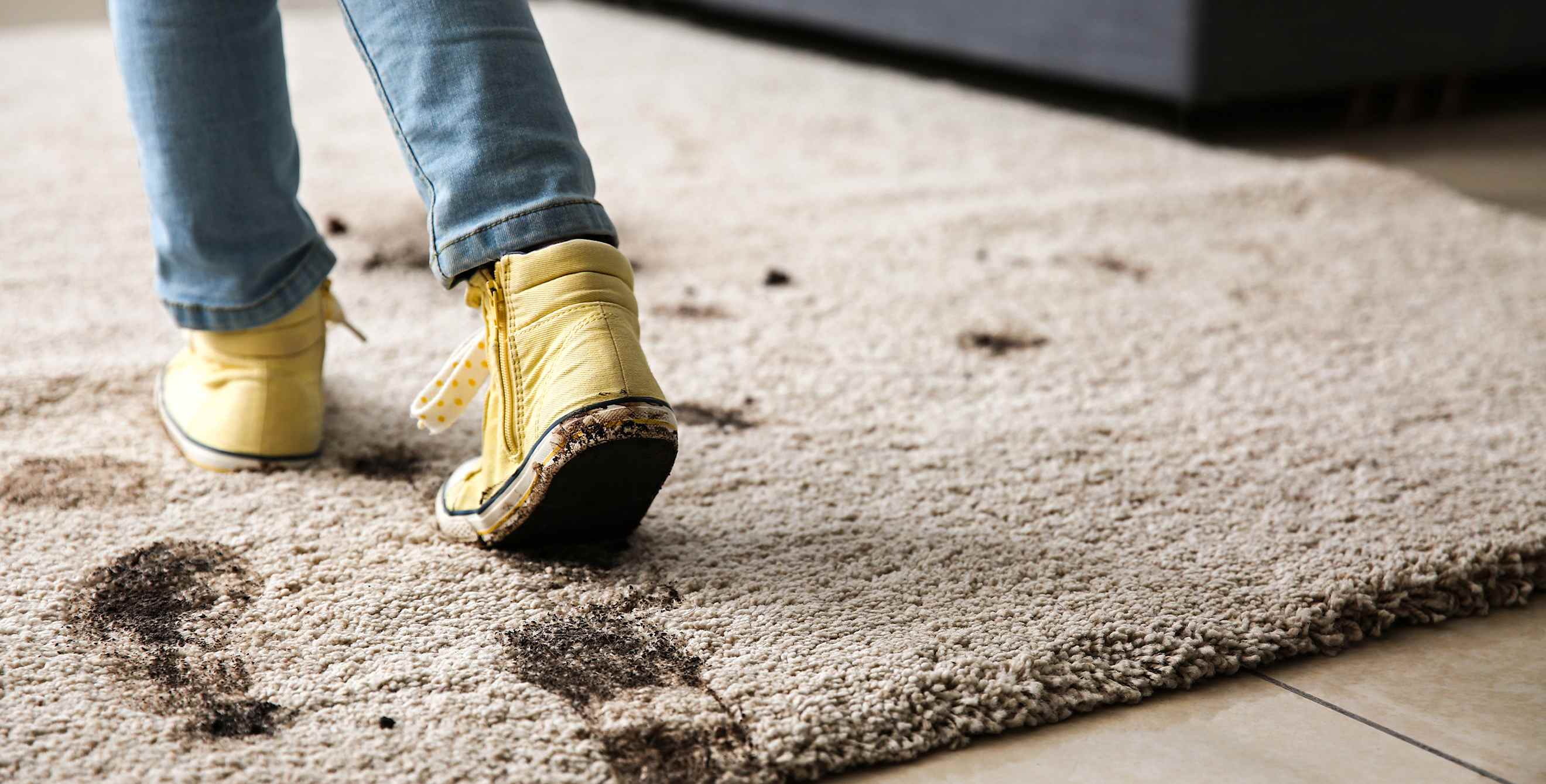 A child walks across a tan rug in dirty shoes.