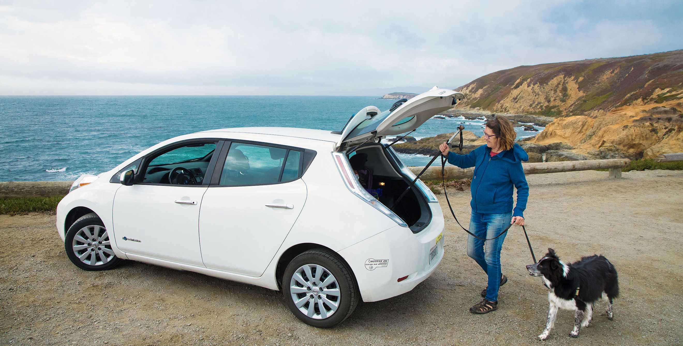 A woman loads hiking poles into the back of her Nissan Leaf EV.