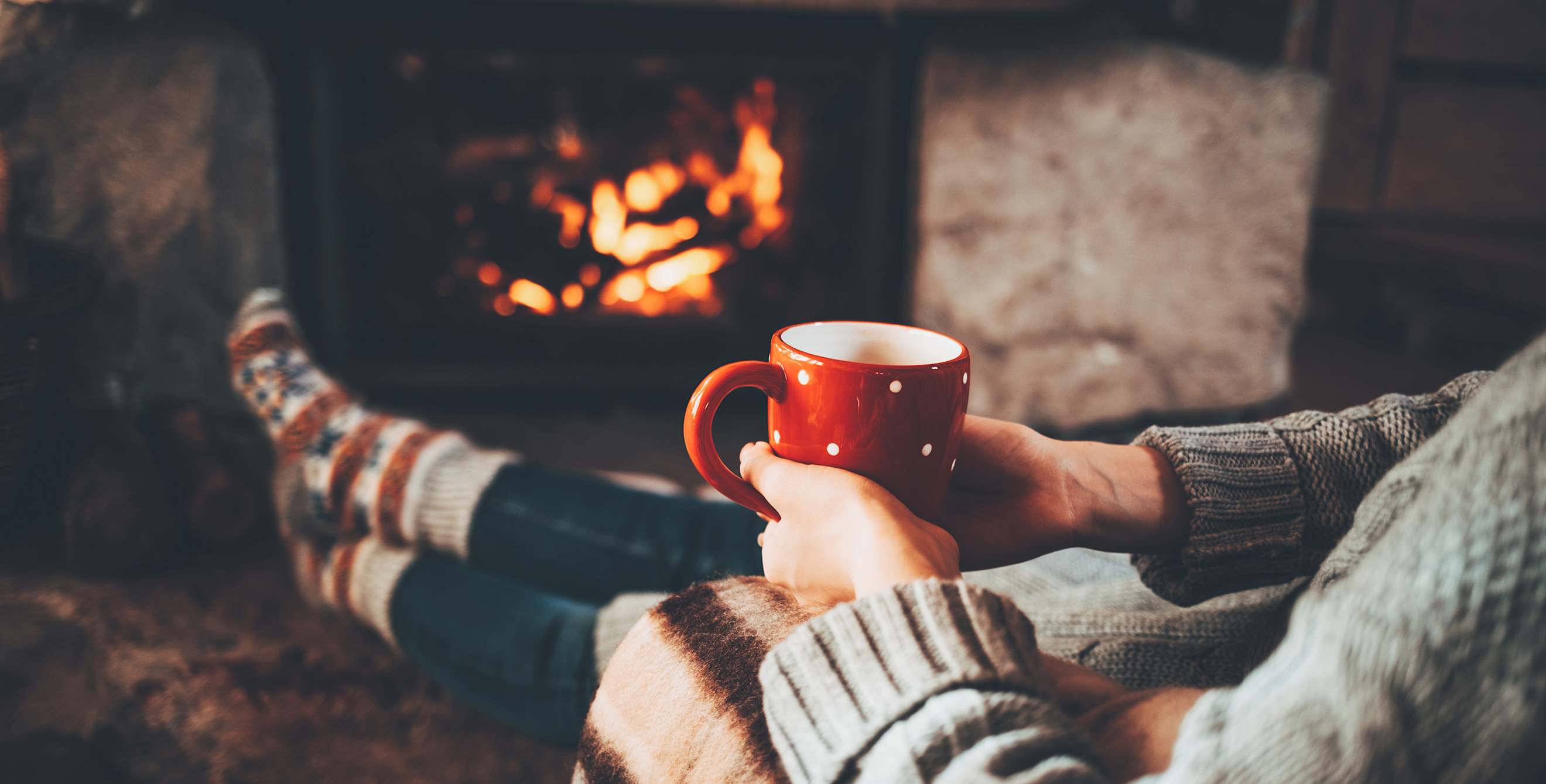 A peson sits in front of the fireplace with a mug of hot chocolate.