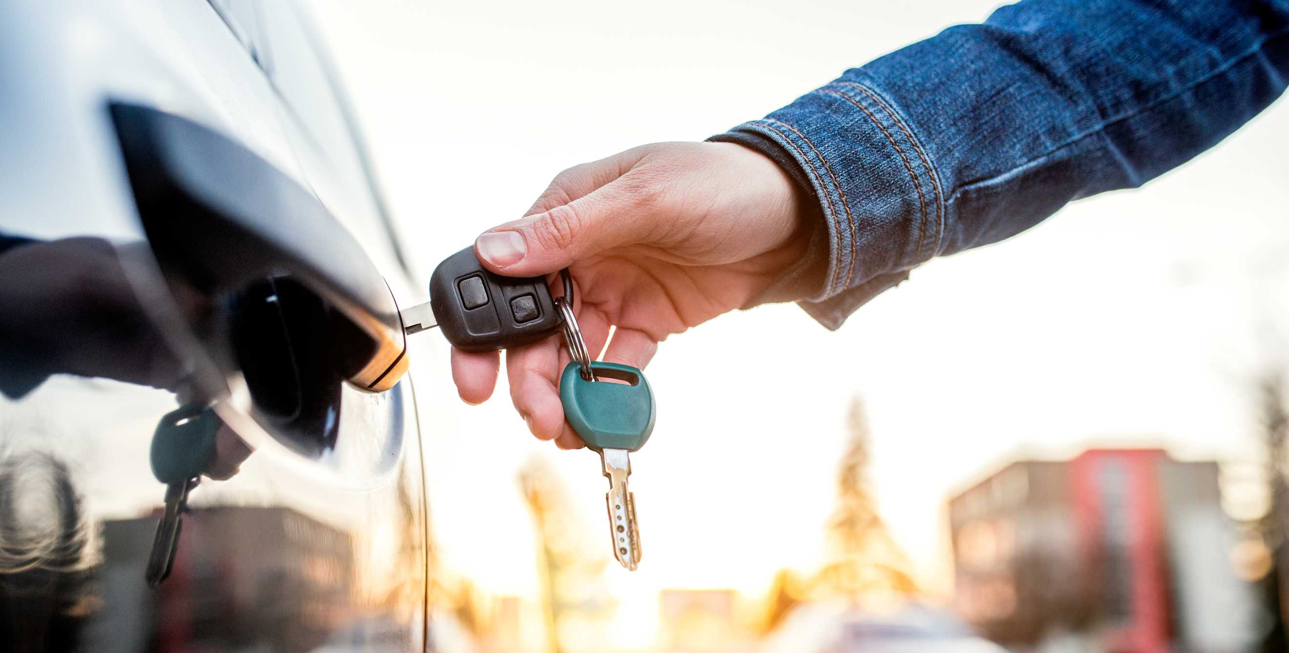 A person locks their car door with the key.