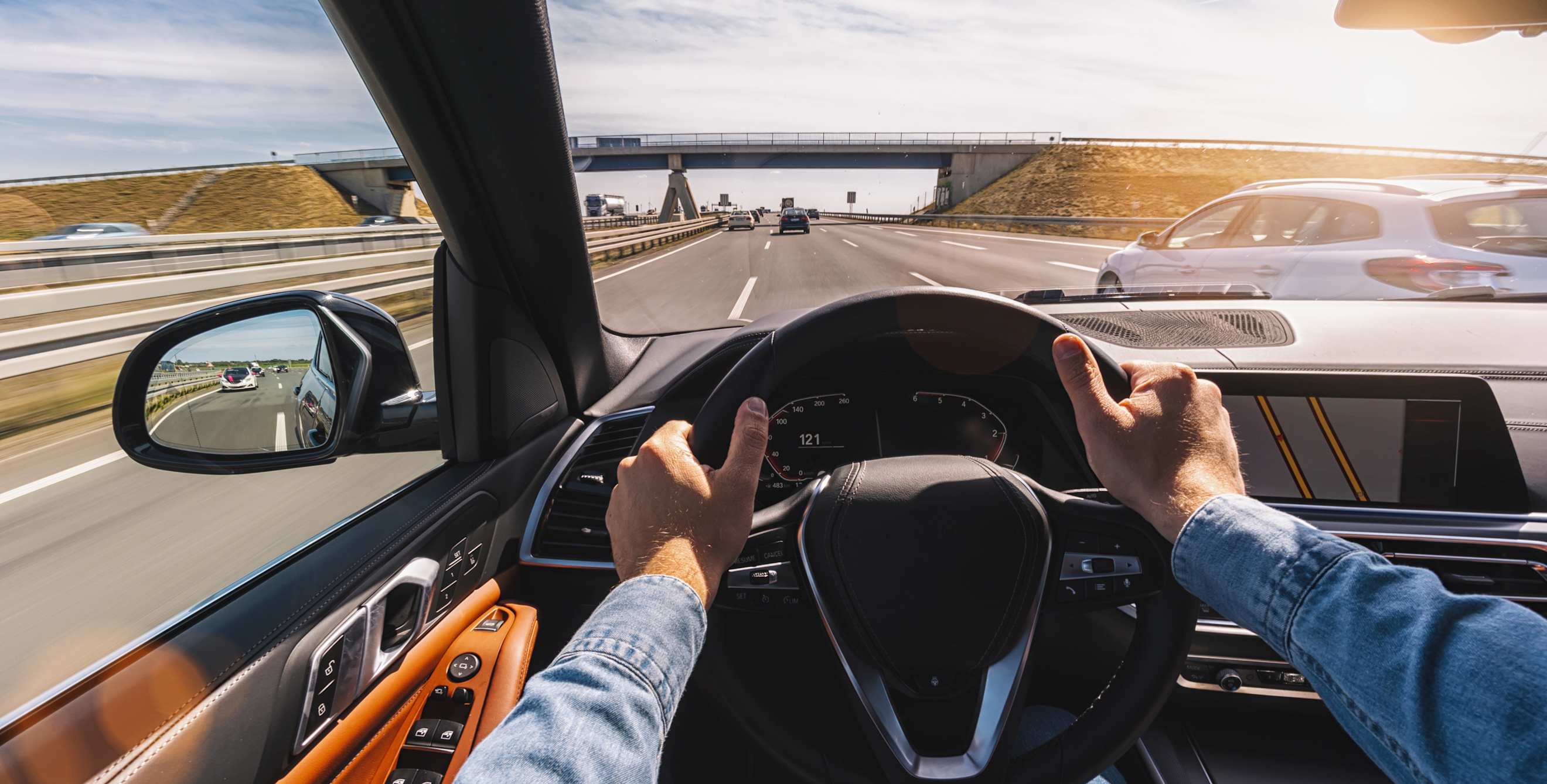 A man drives on the highway with both hands on the wheel.