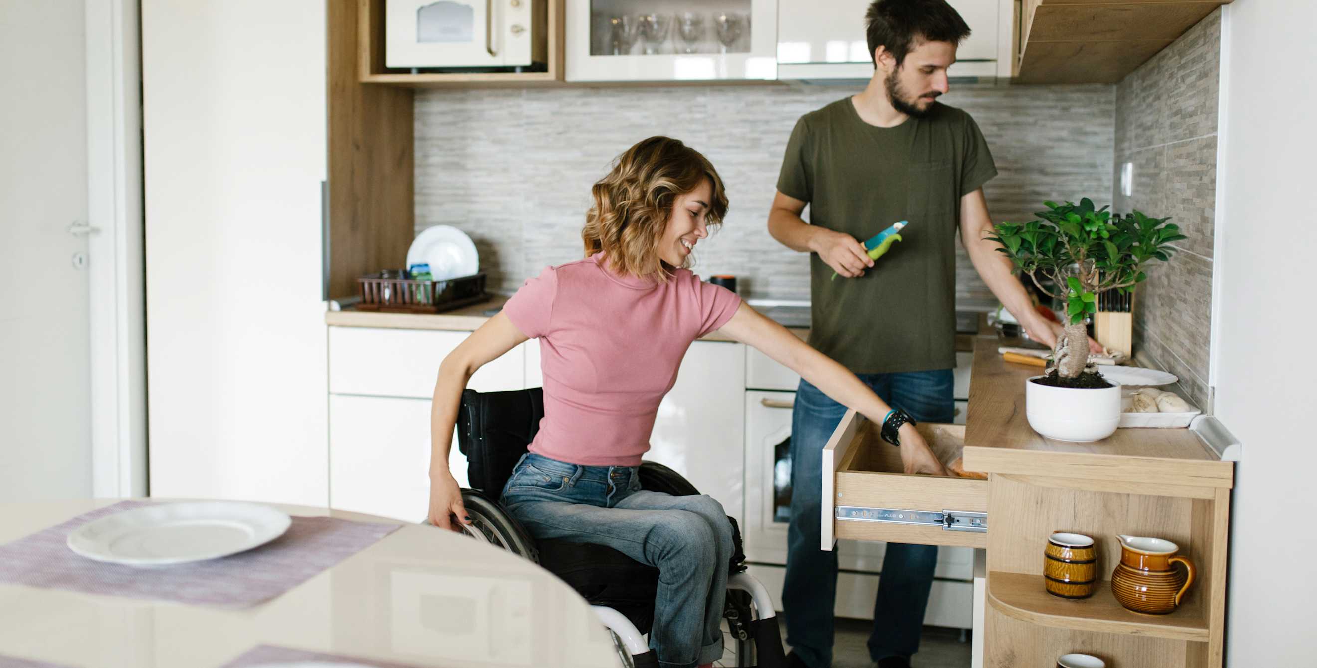 A woman in a wheelchair gets silverware out of a kitchen drawer.