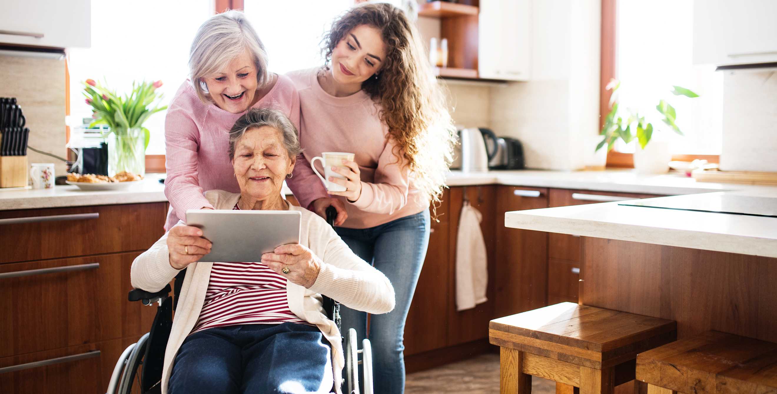 Three generations look over a grandmother's shoulder at a tablet.