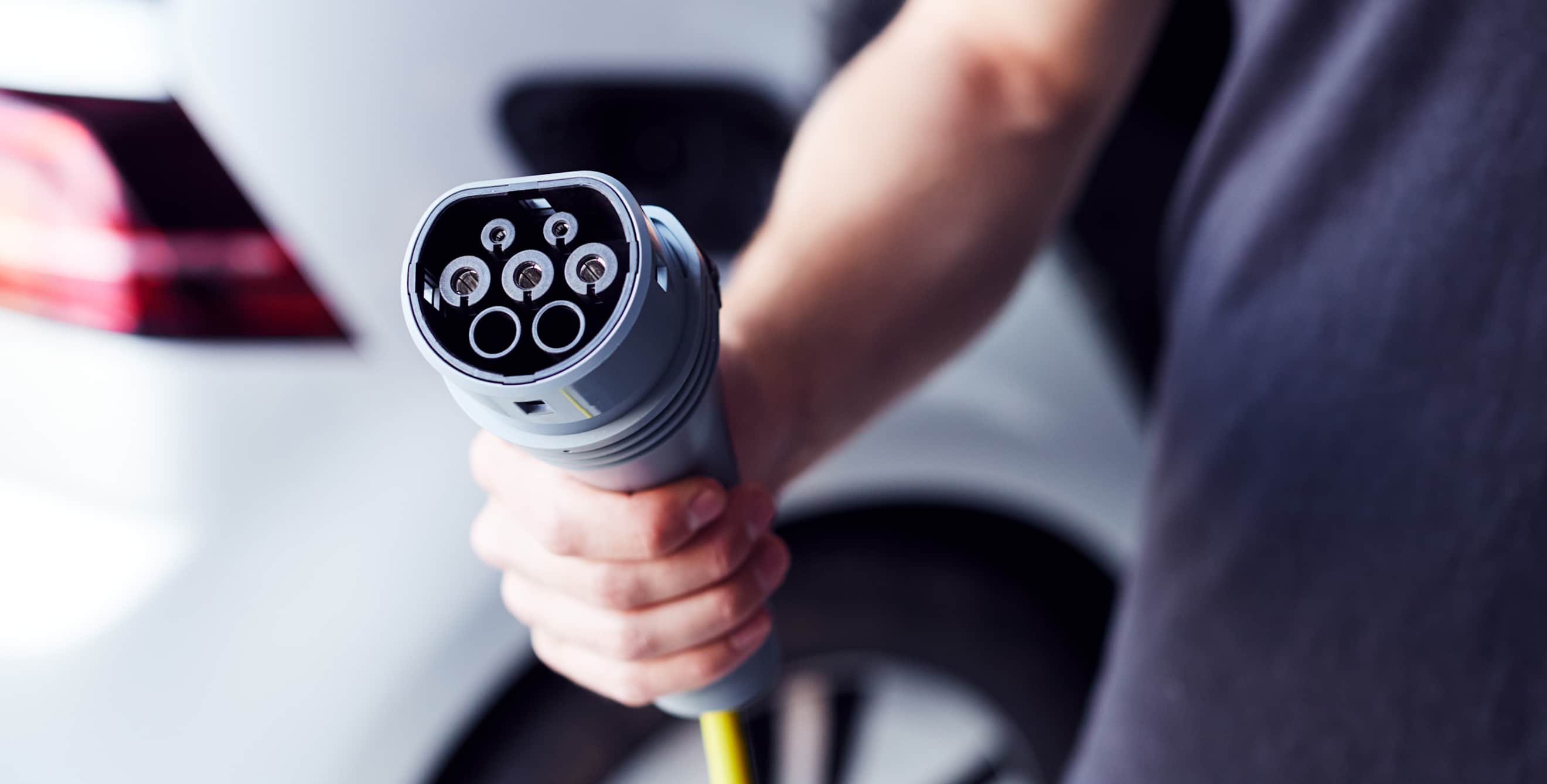 A person holds an EV charger in their garage.