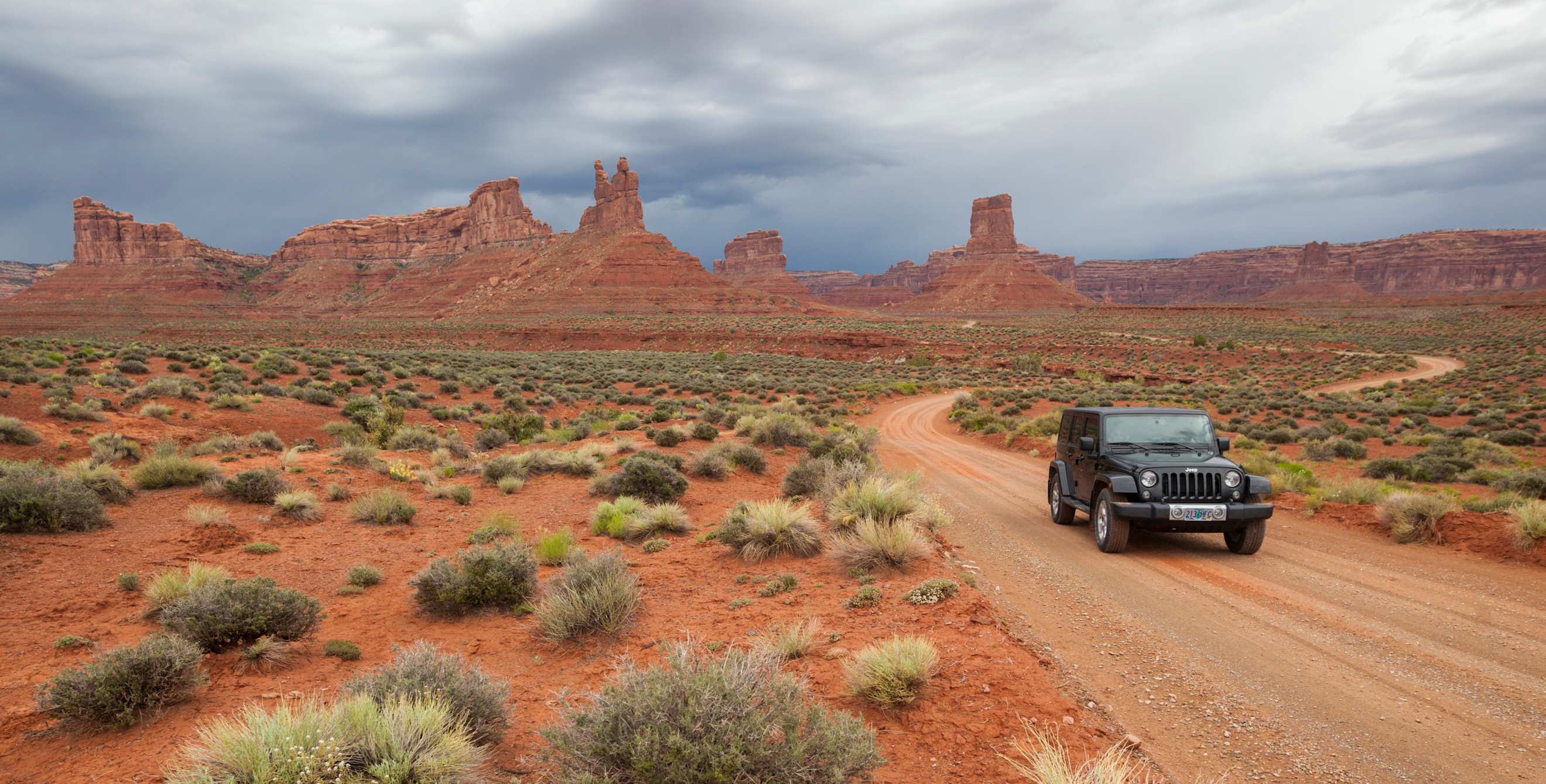 A Jeep drives on a dirt road through Valley of the Gods in Utah.