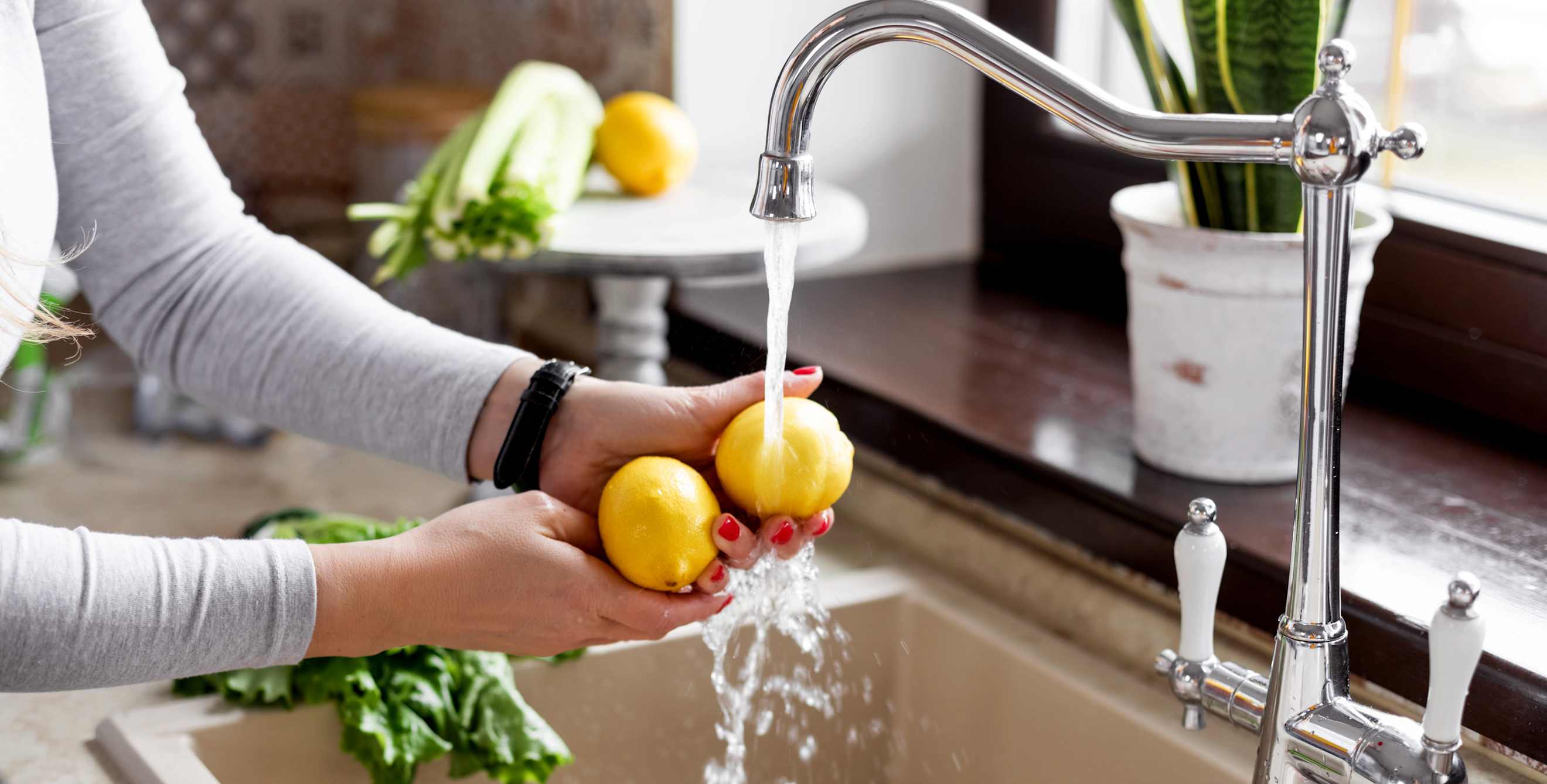 A woman washes lemon at the kitchen sink.