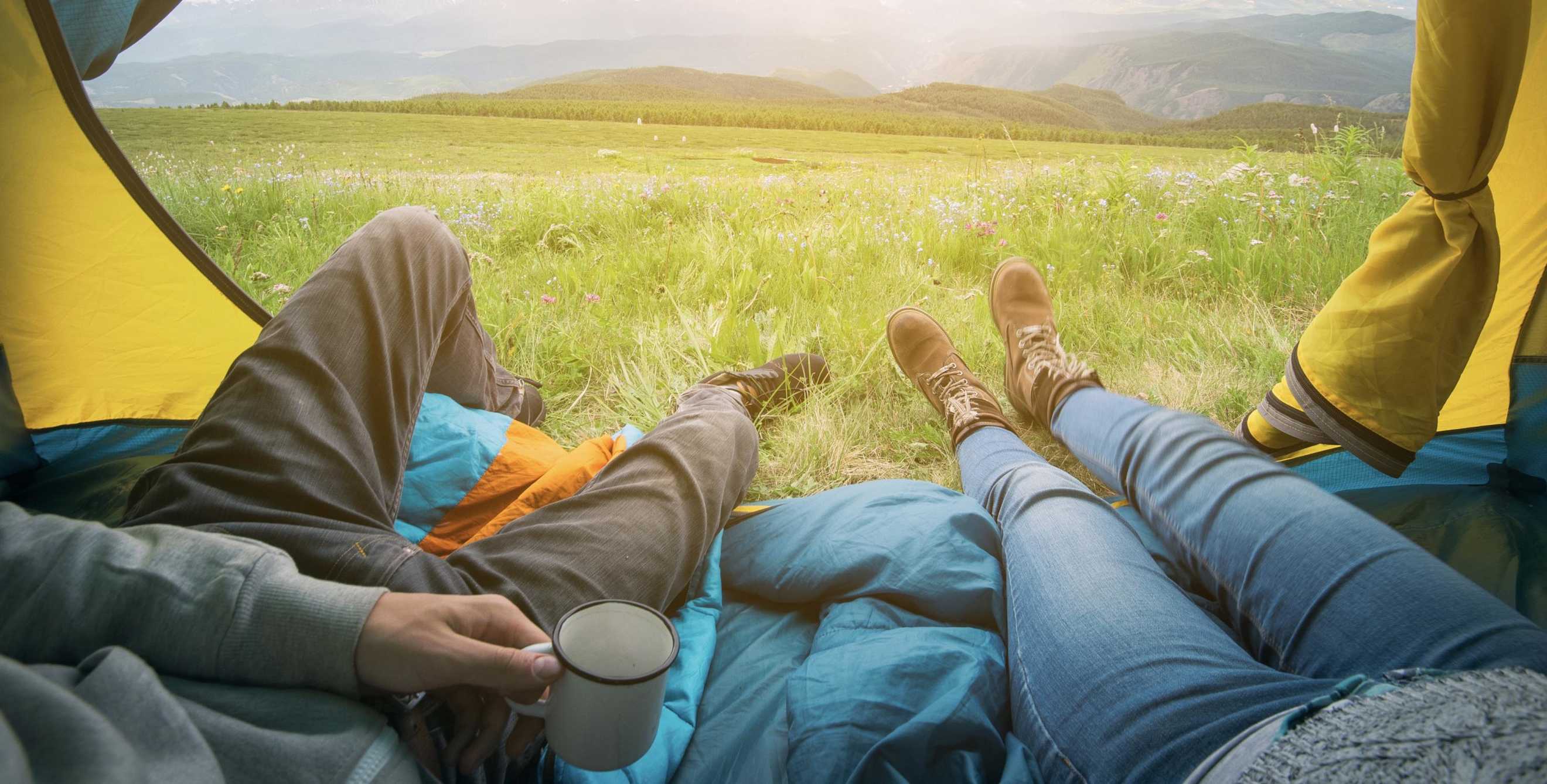 picture of a couple camping, looking out their tent at beautiful view