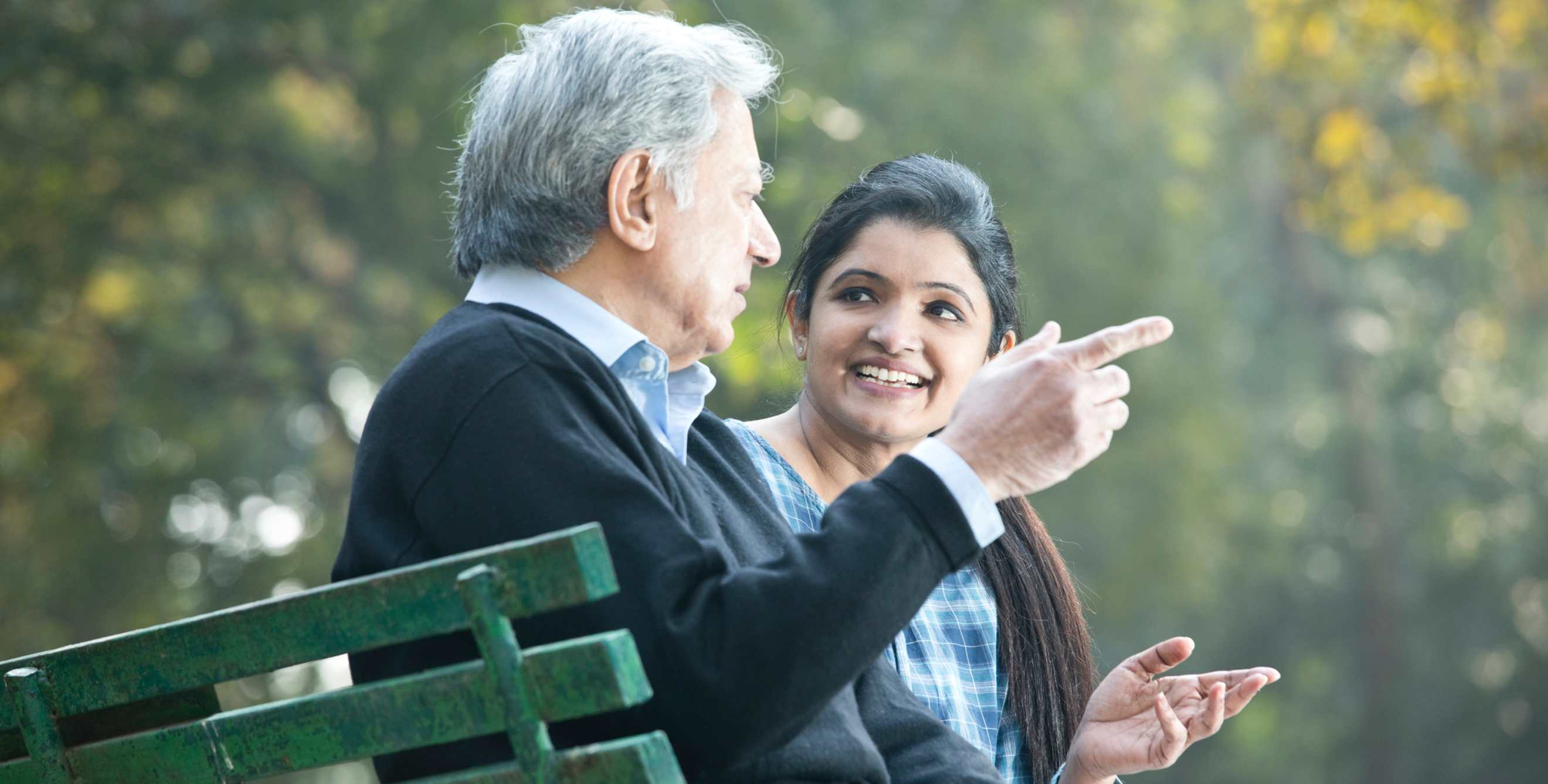 A father and daughter talk while sitting on a park bench.