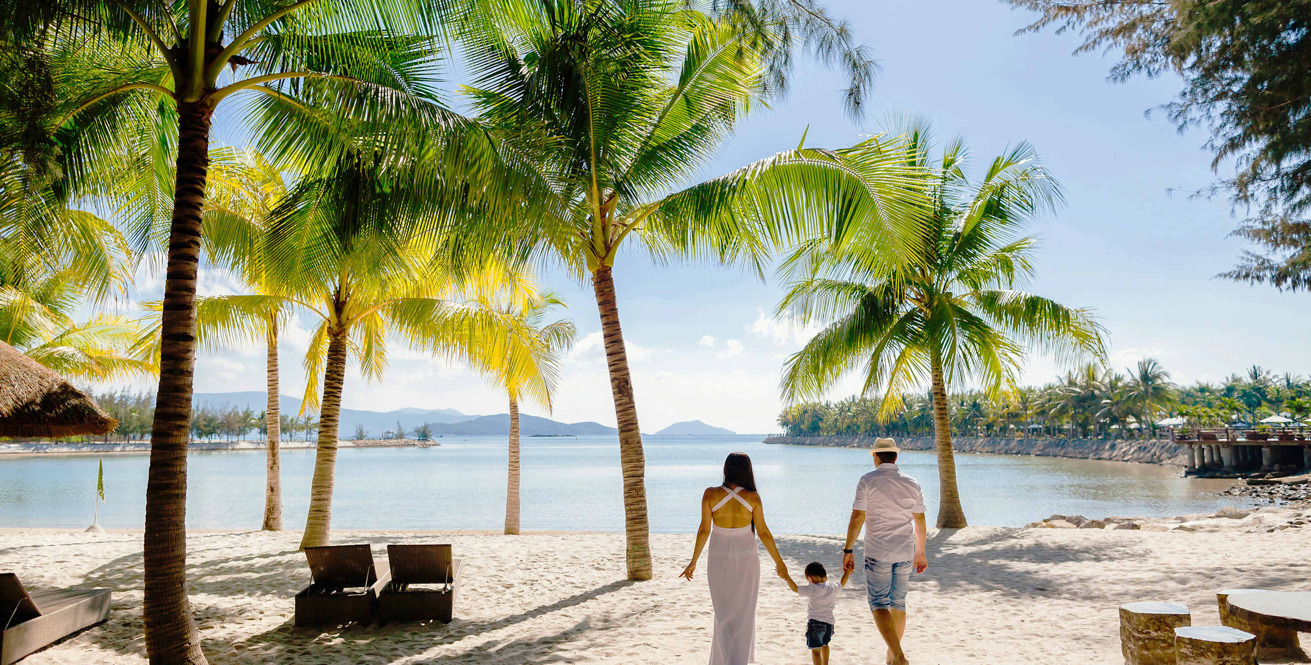 A family walks together on a white sand tropical beach.