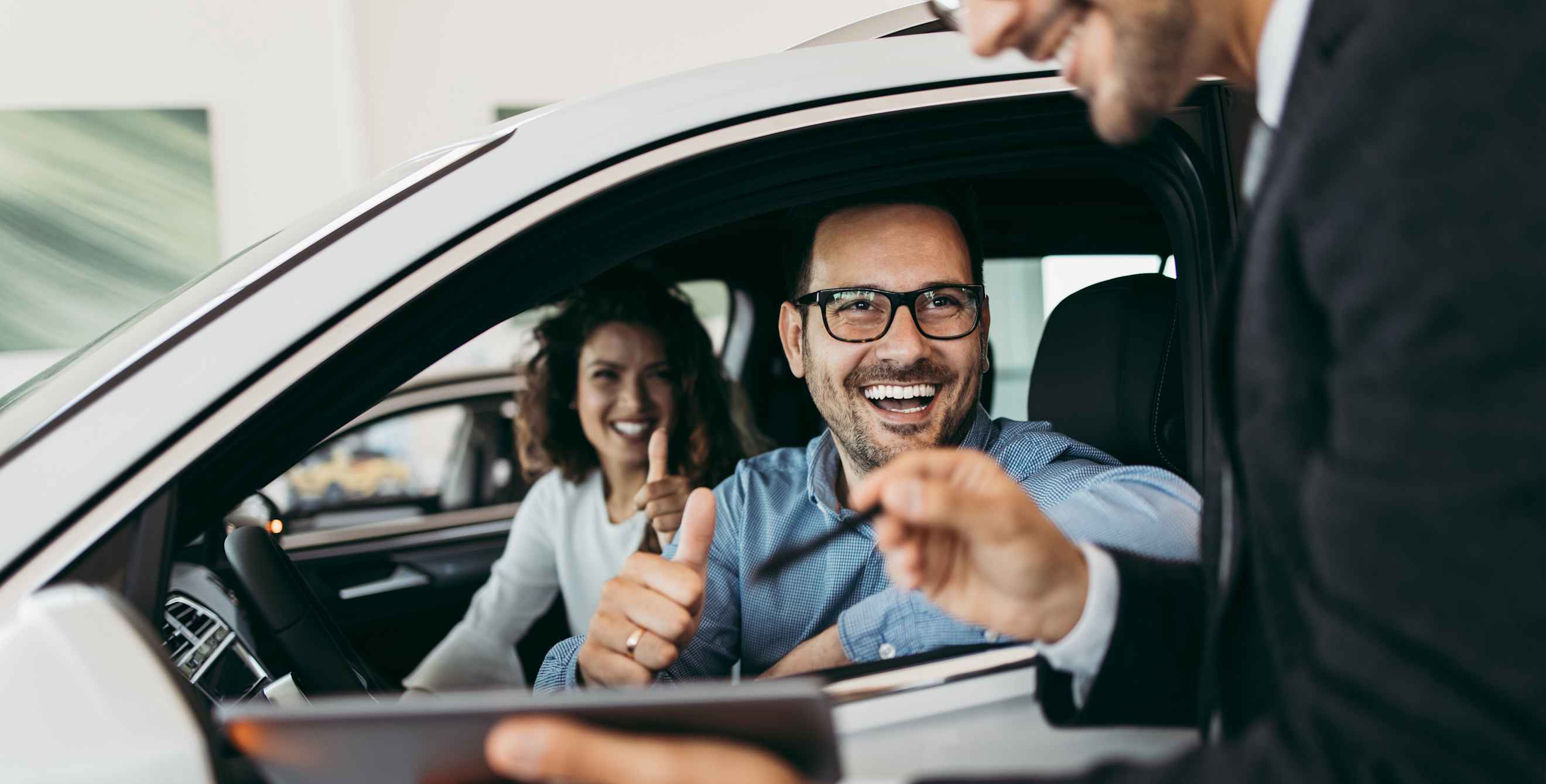 A couple sit in a new car inside the dealership.