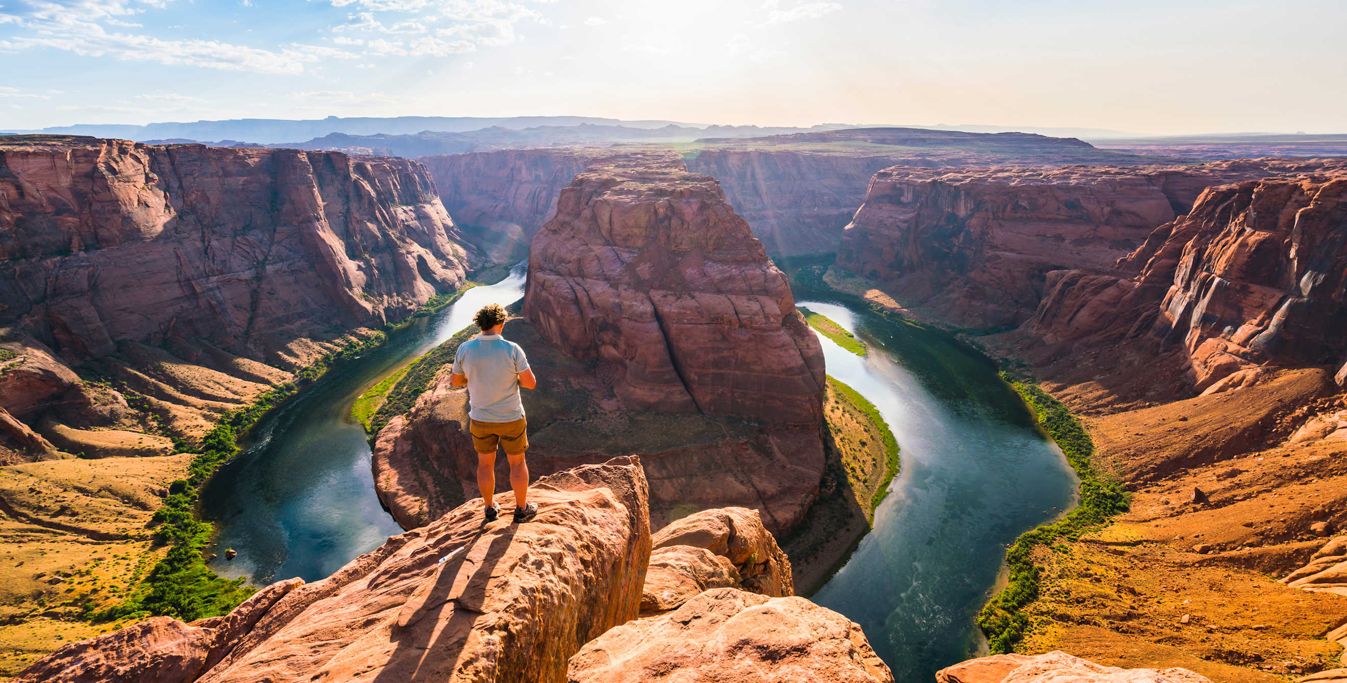A tourist stands overlooking Horseshoe Bend on sunny day in Page, Arizona.