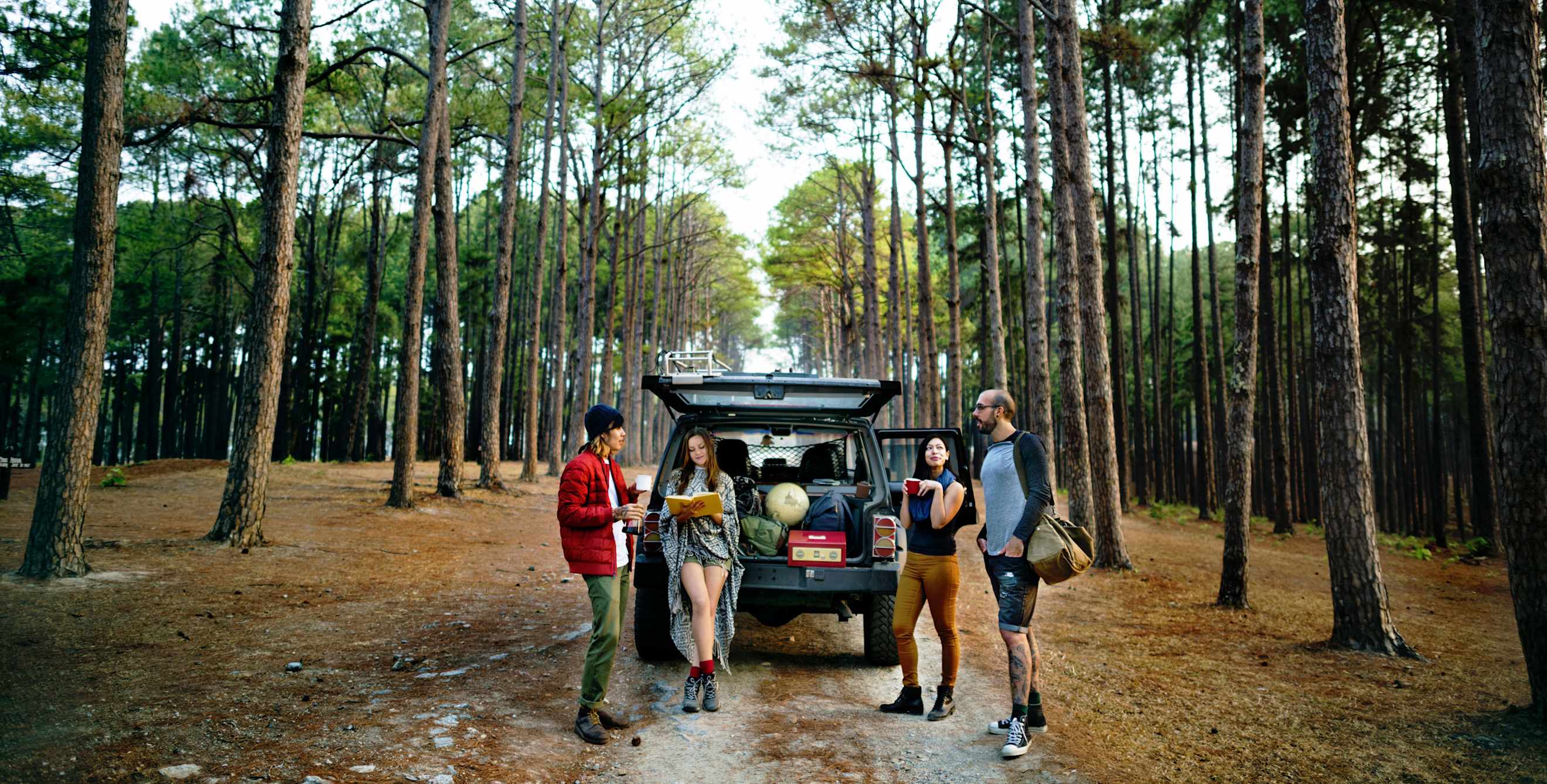 Friends stand around an open car tailgate with camping gear in the back, image
