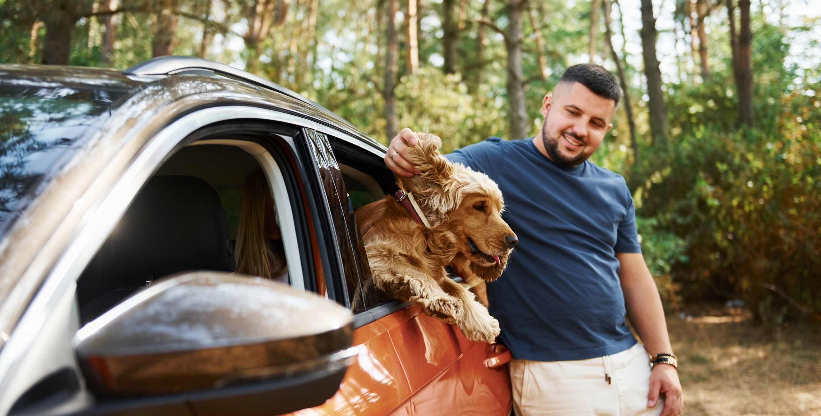 A man stands outside his car and pets his dog in the backseat.