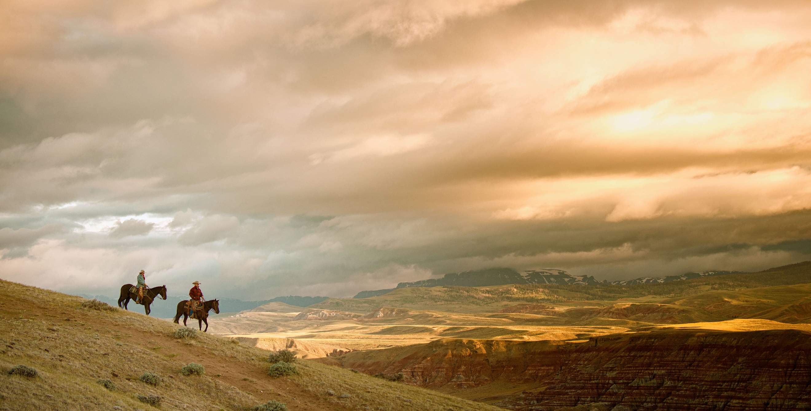 Two people horseback riding in the Dubois Badlands on a cloudy day.