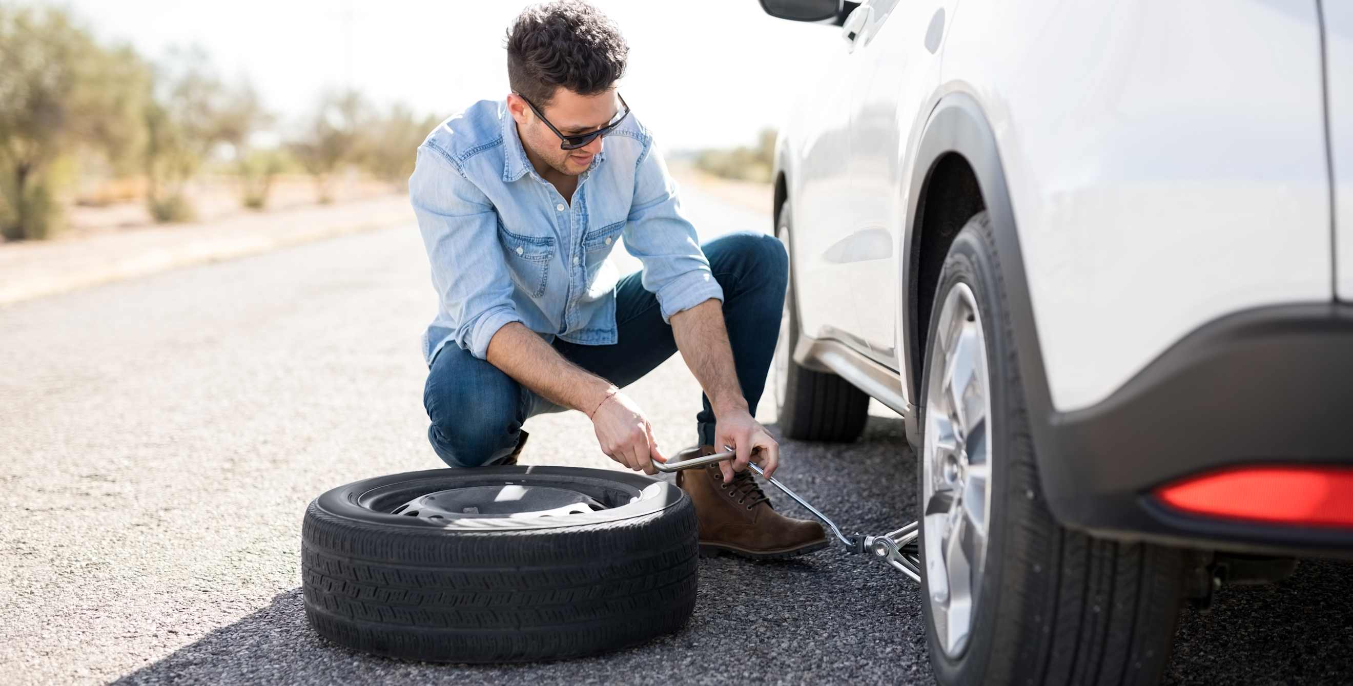 A driver jacks up their SUV to install a spare tire.