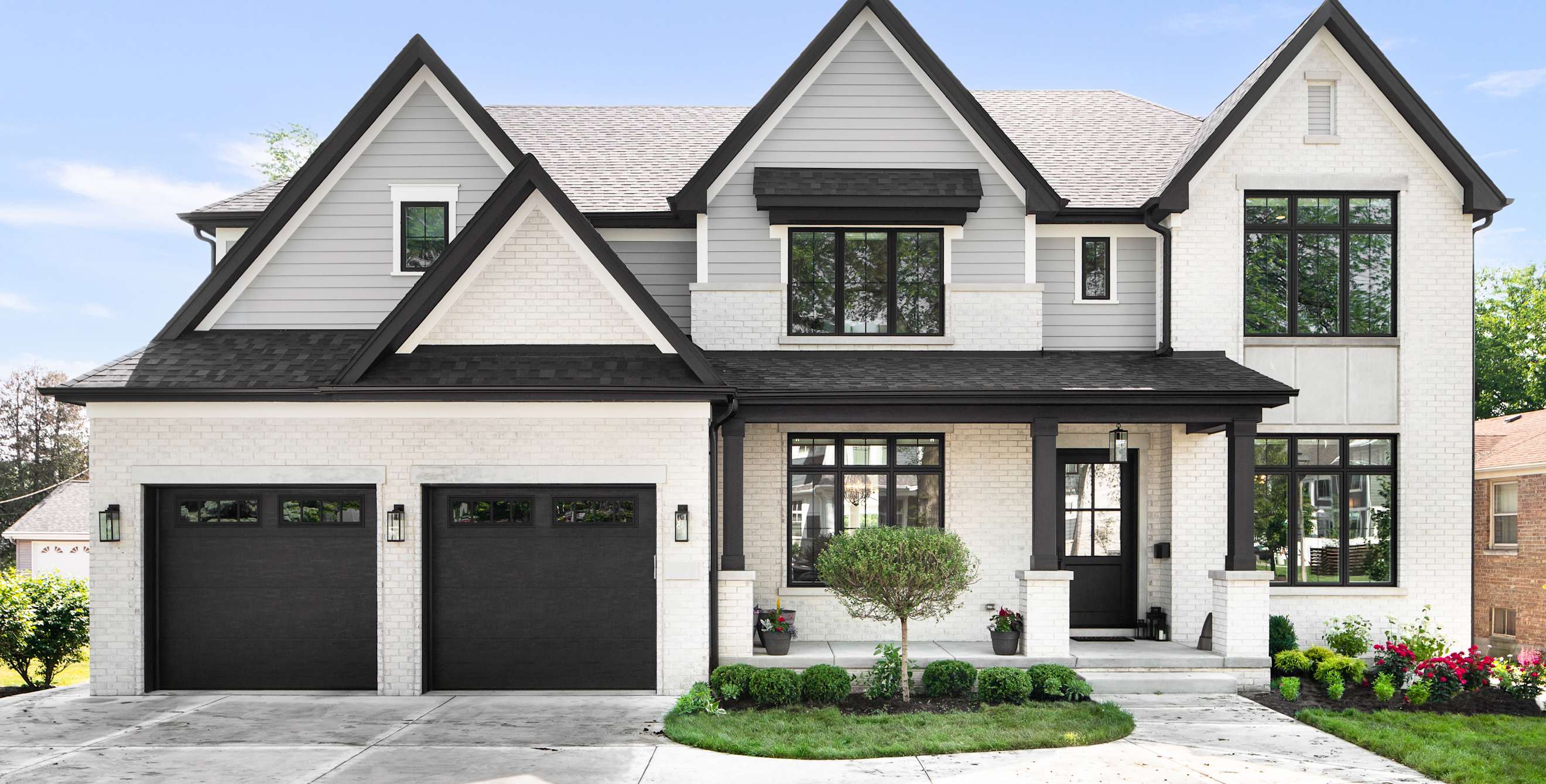 A beautiful modern farmhouse with grey siding, white brick, and black framed windows.