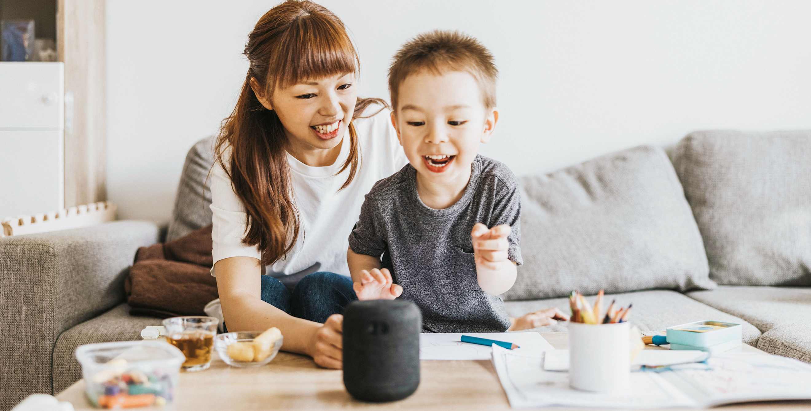 A mom and her son use a smart speaker while coloring.