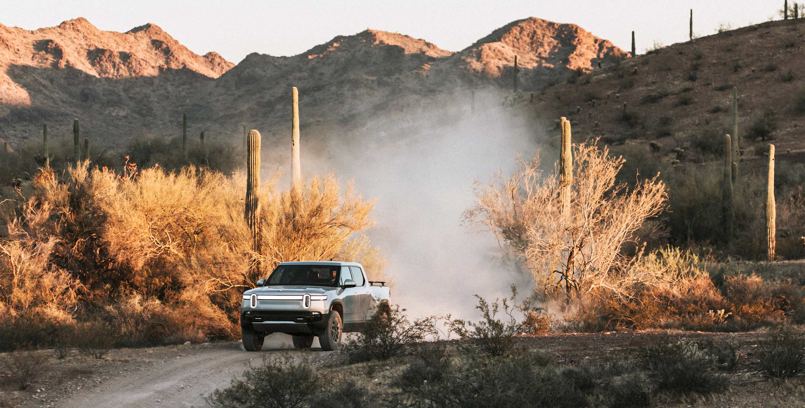 A Rivian truck drives off-road in the desert.