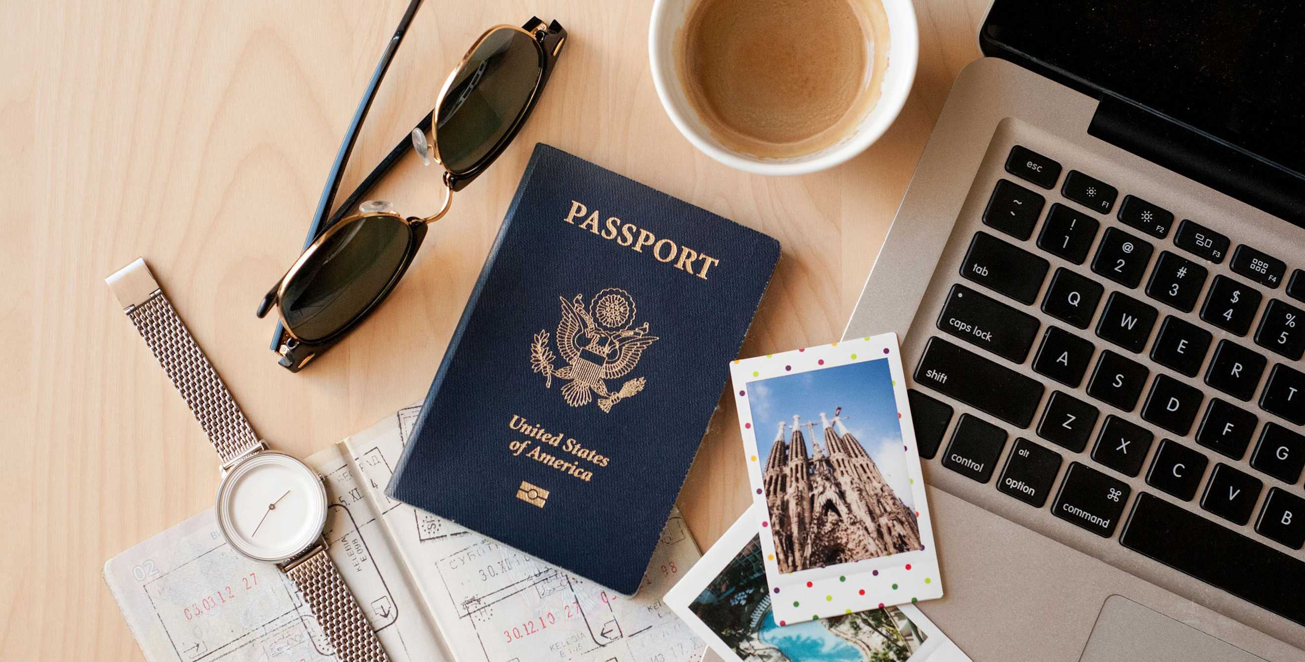 A passport and photos lay on a desk next to a laptop.