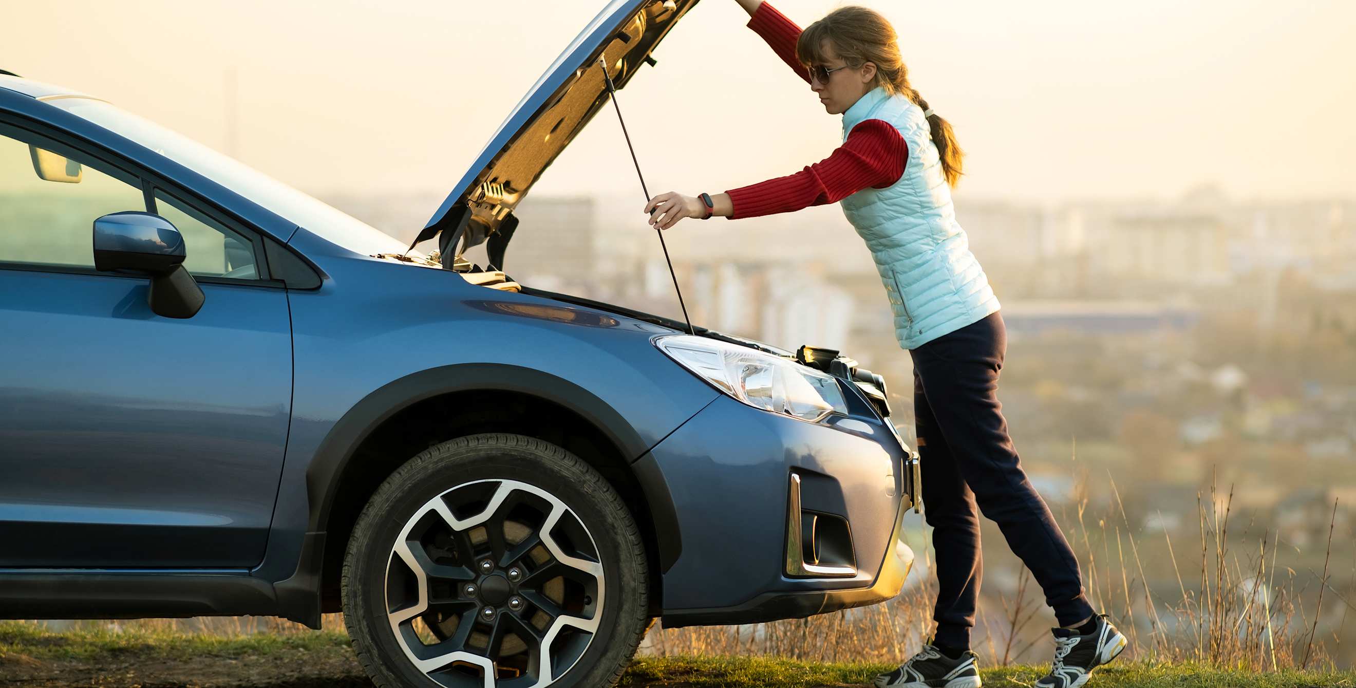 A woman holds open the hood on her Subaru to check her alternator.