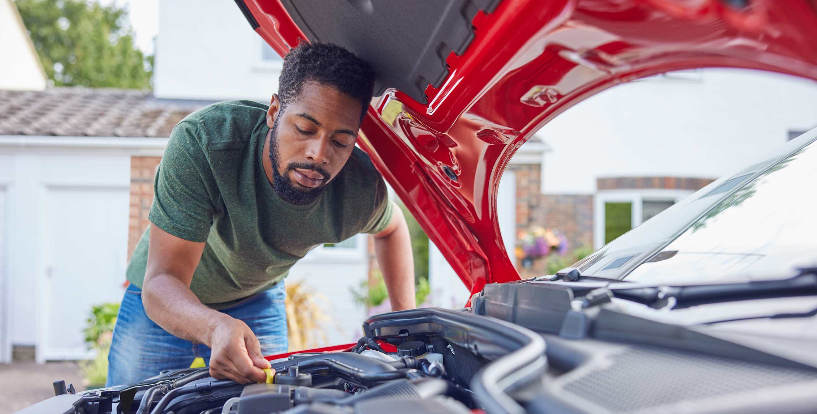 A man checks the oil on his red sedan.