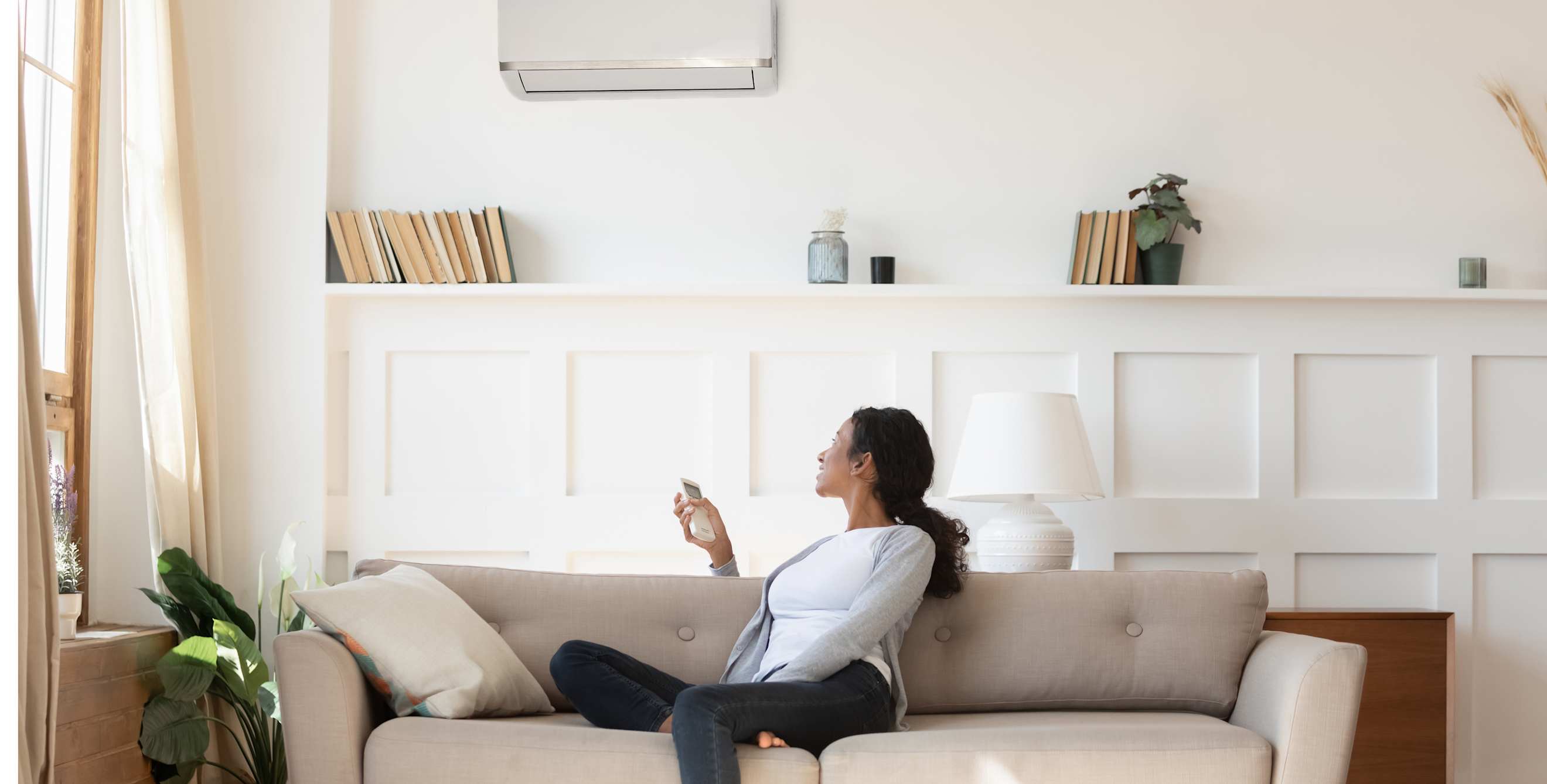 A woman turns on her mini split heat pump while sitting on the couch in the living room.