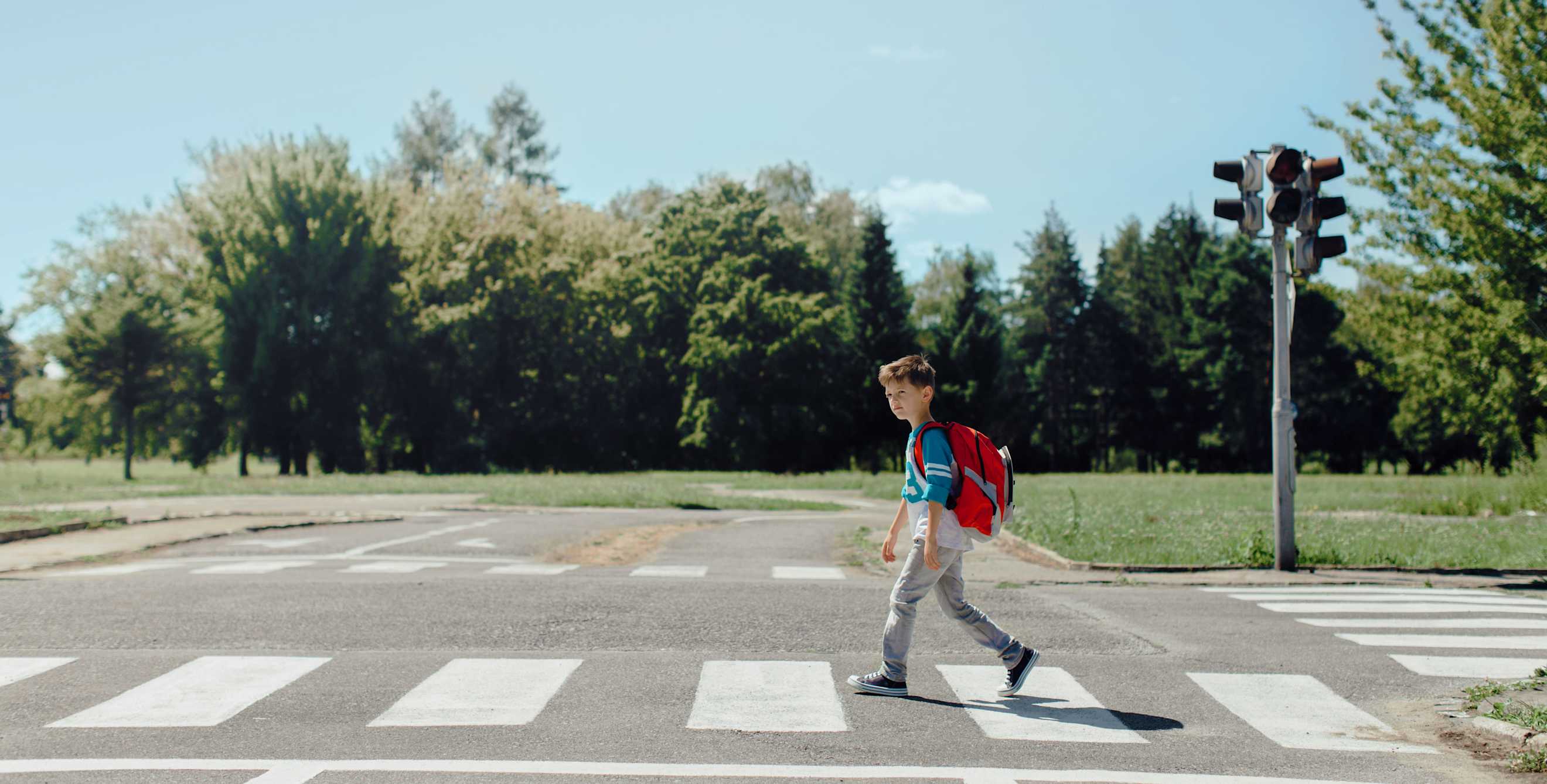 A young boy crosses a crosswalk on a sunny day.