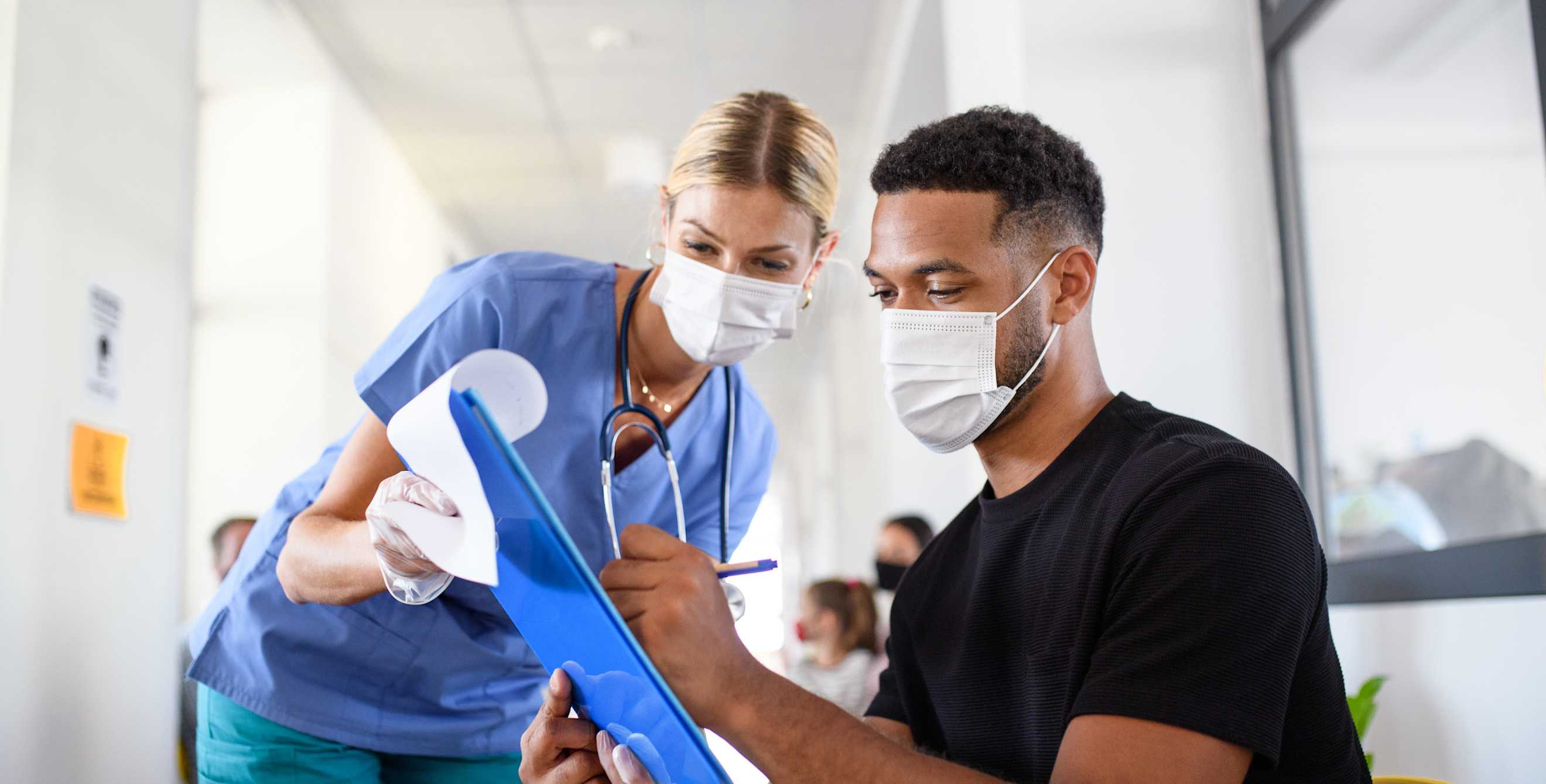 A nurse helps a patient fill out a form in waiting room.