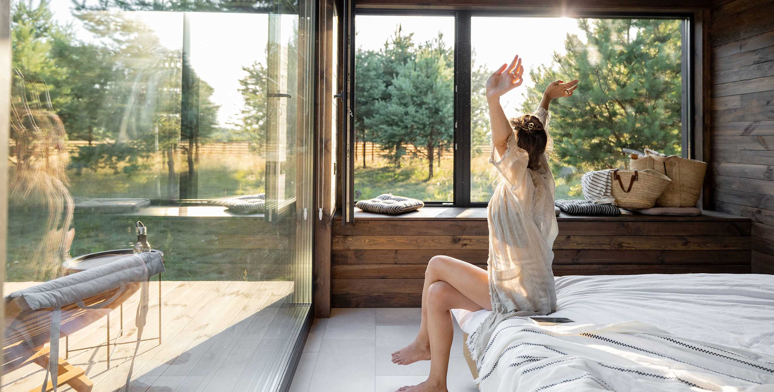 A woman stretches at the foot of her bed as morning light streams into her hotel room.