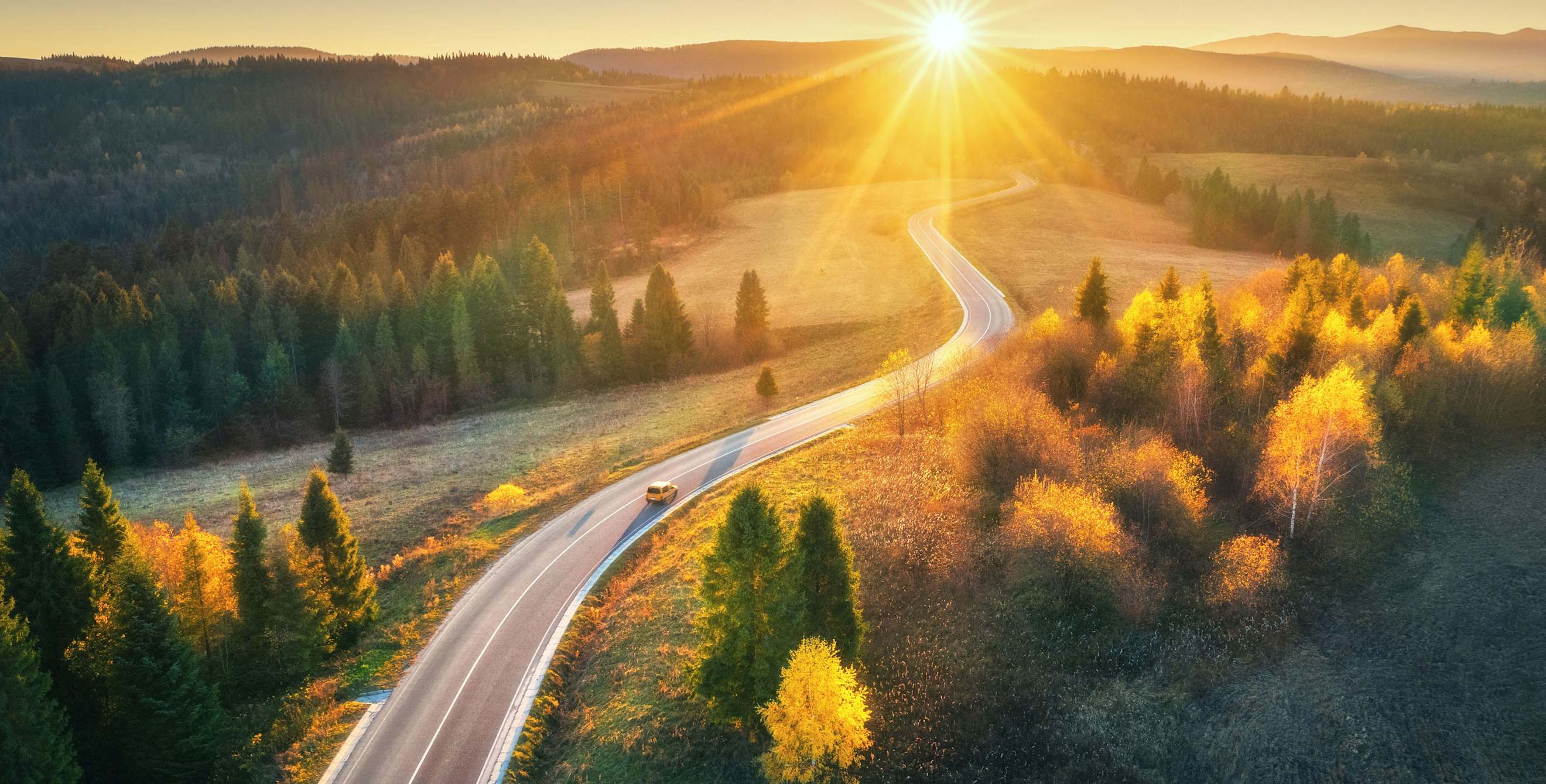 A car drives down a rural road at sunset.