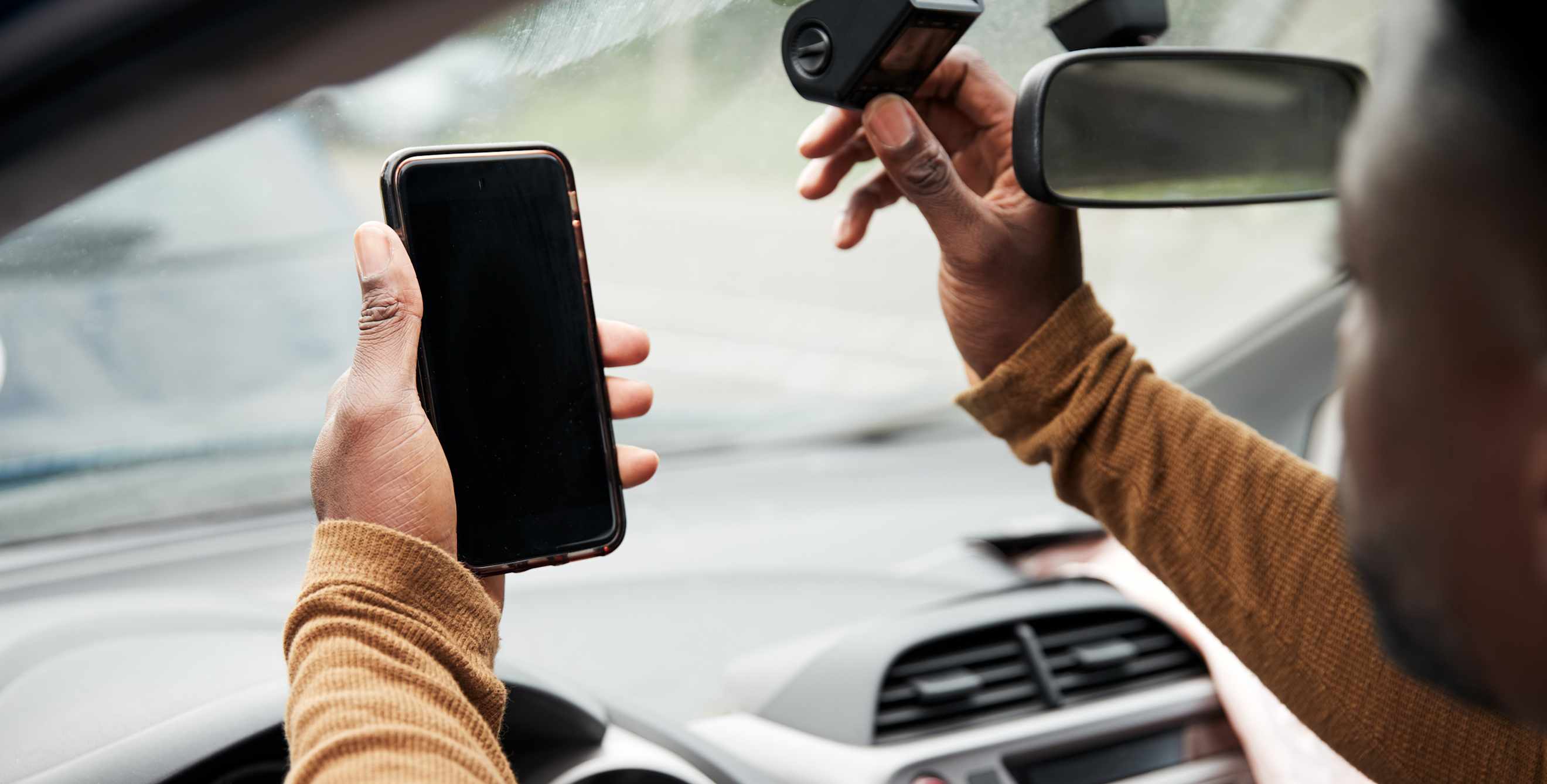 A driver installs a dash cam behind their rear view mirror.