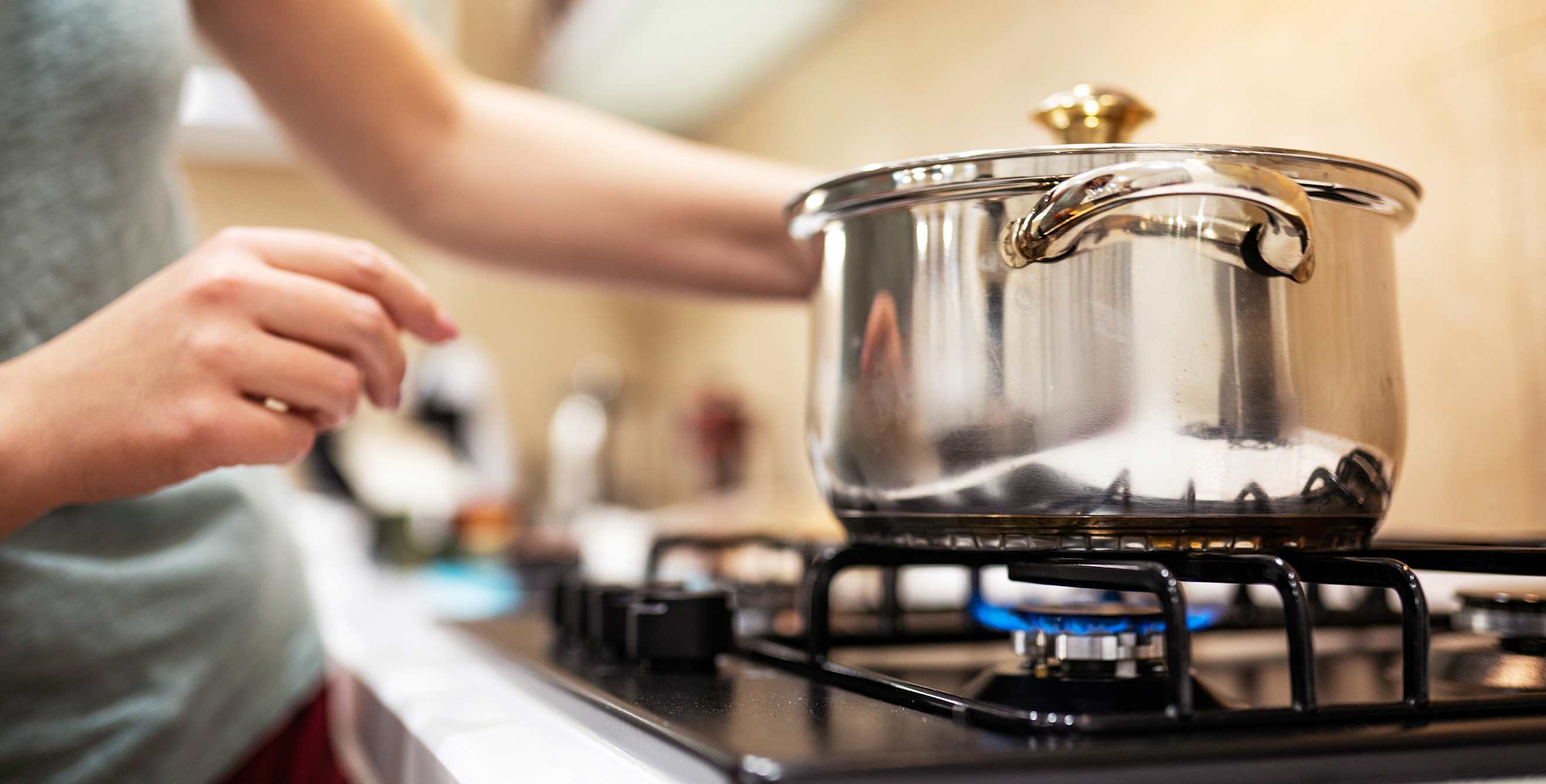 A woman lights the stove under a large pot.