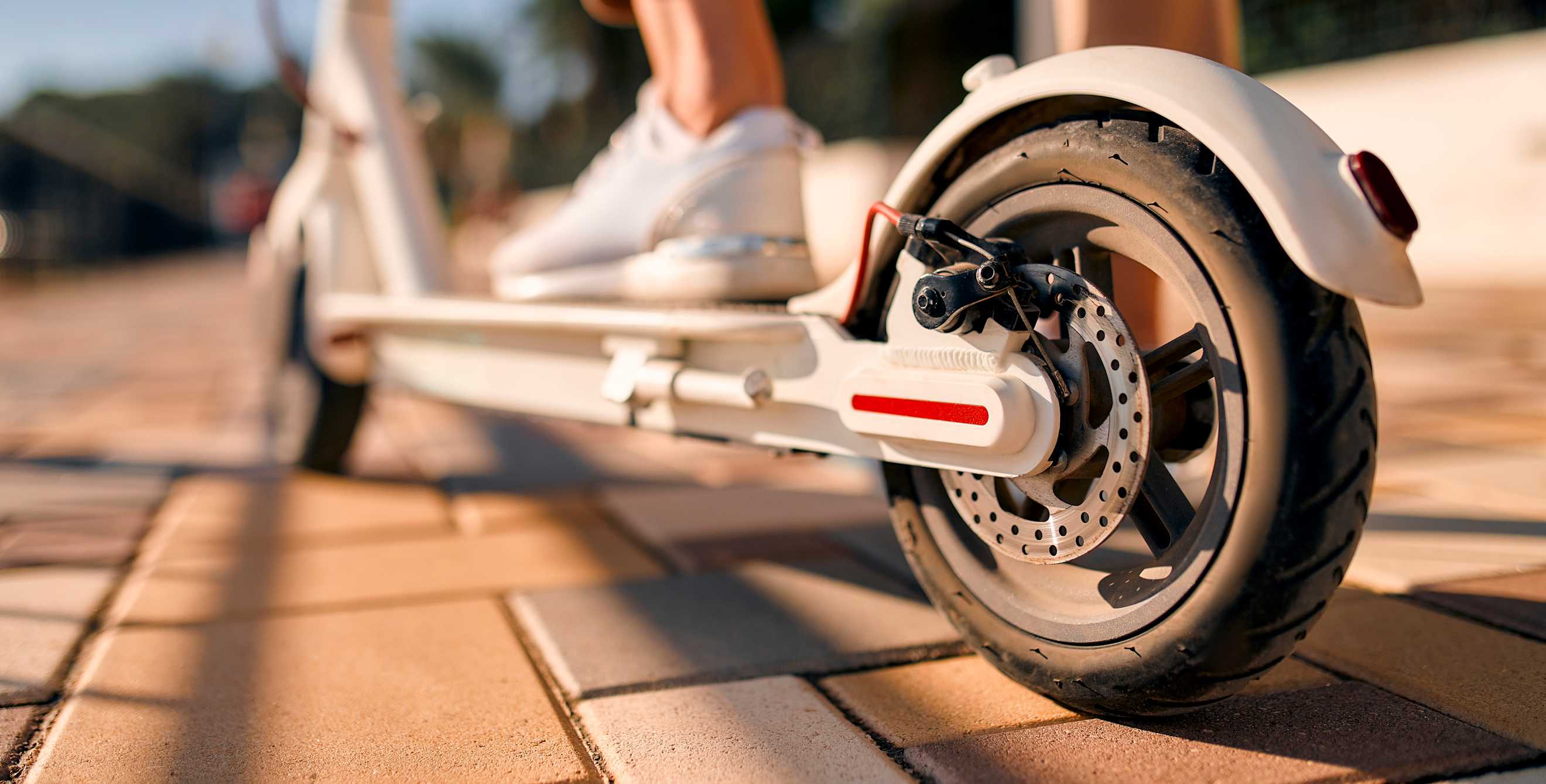 A person stands on an electric scooter in white sneakers.
