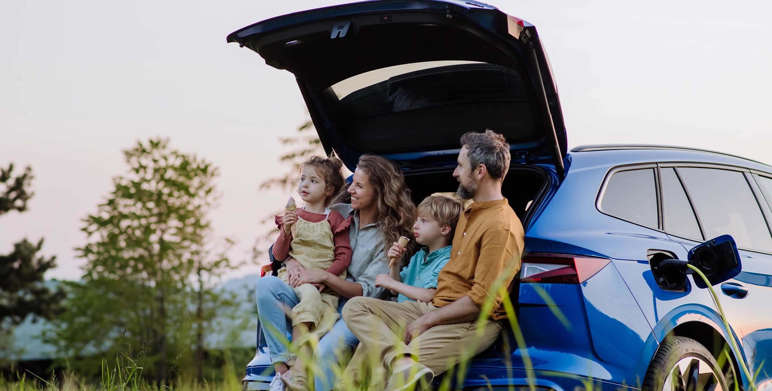 A family sits in the hatchback of their blue electric SUV