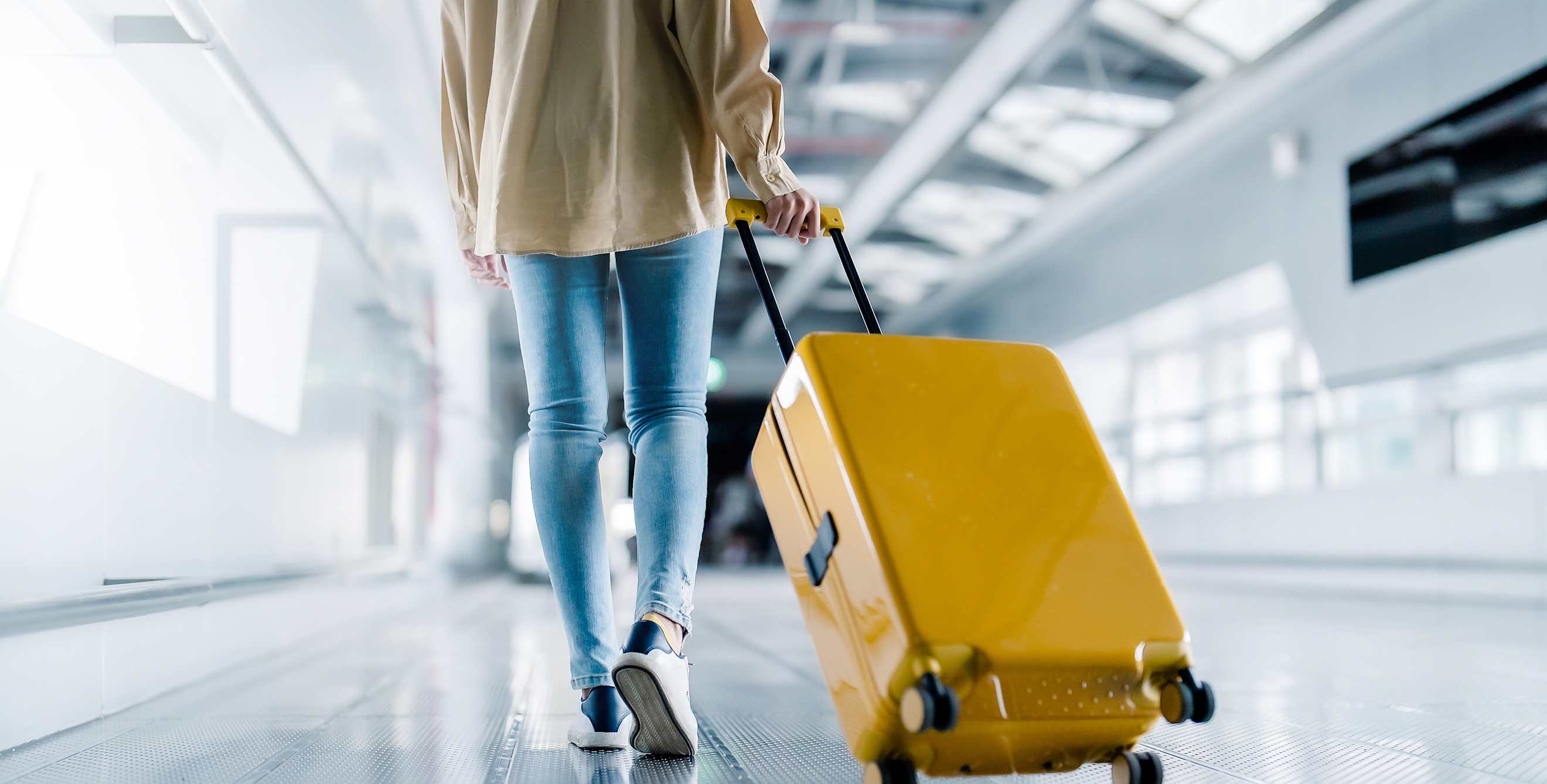 A woman pulls her yellow hard-sided suitcase through the airport.