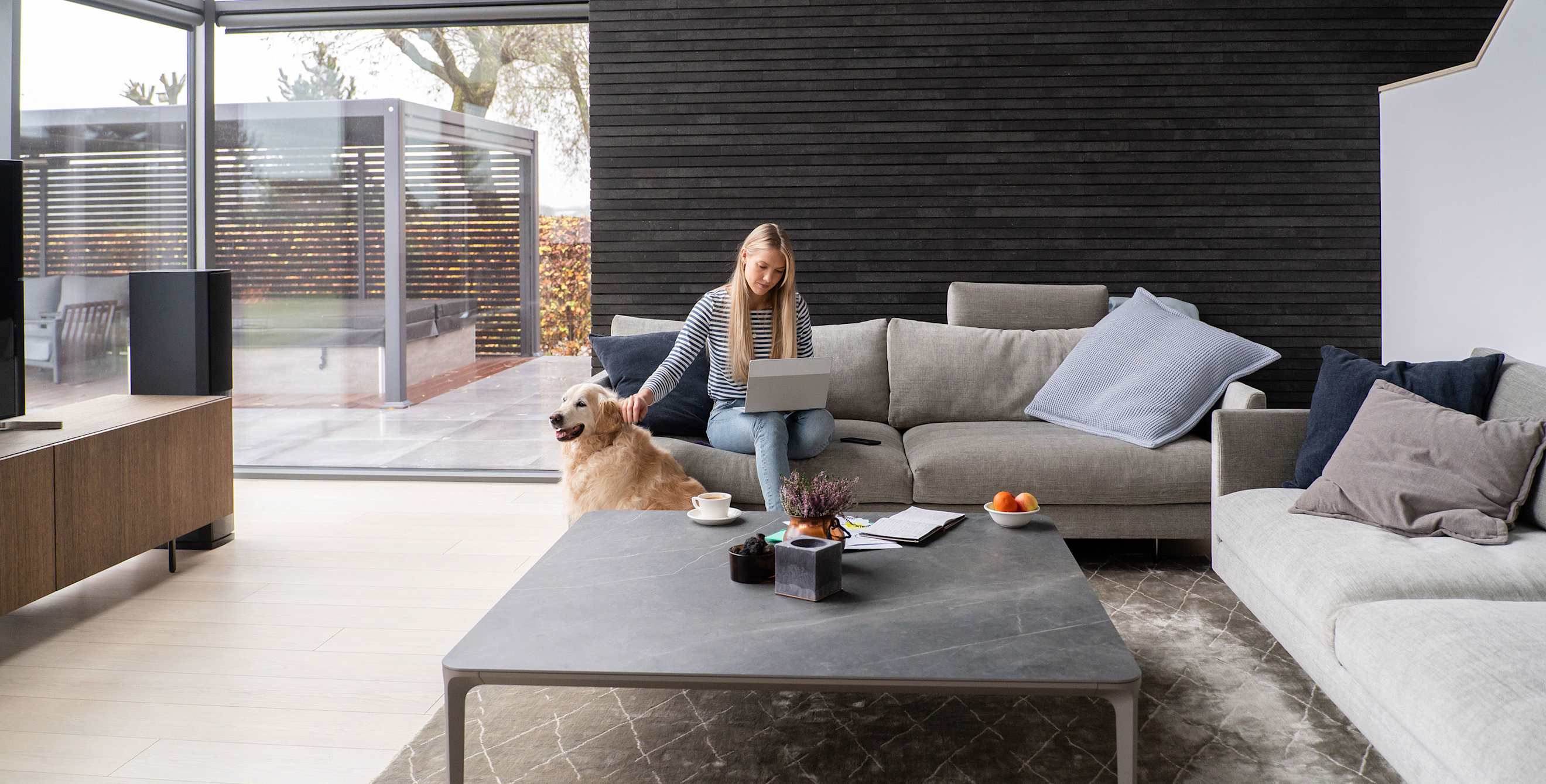 A woman sits on her couch with her dog in a modern home.